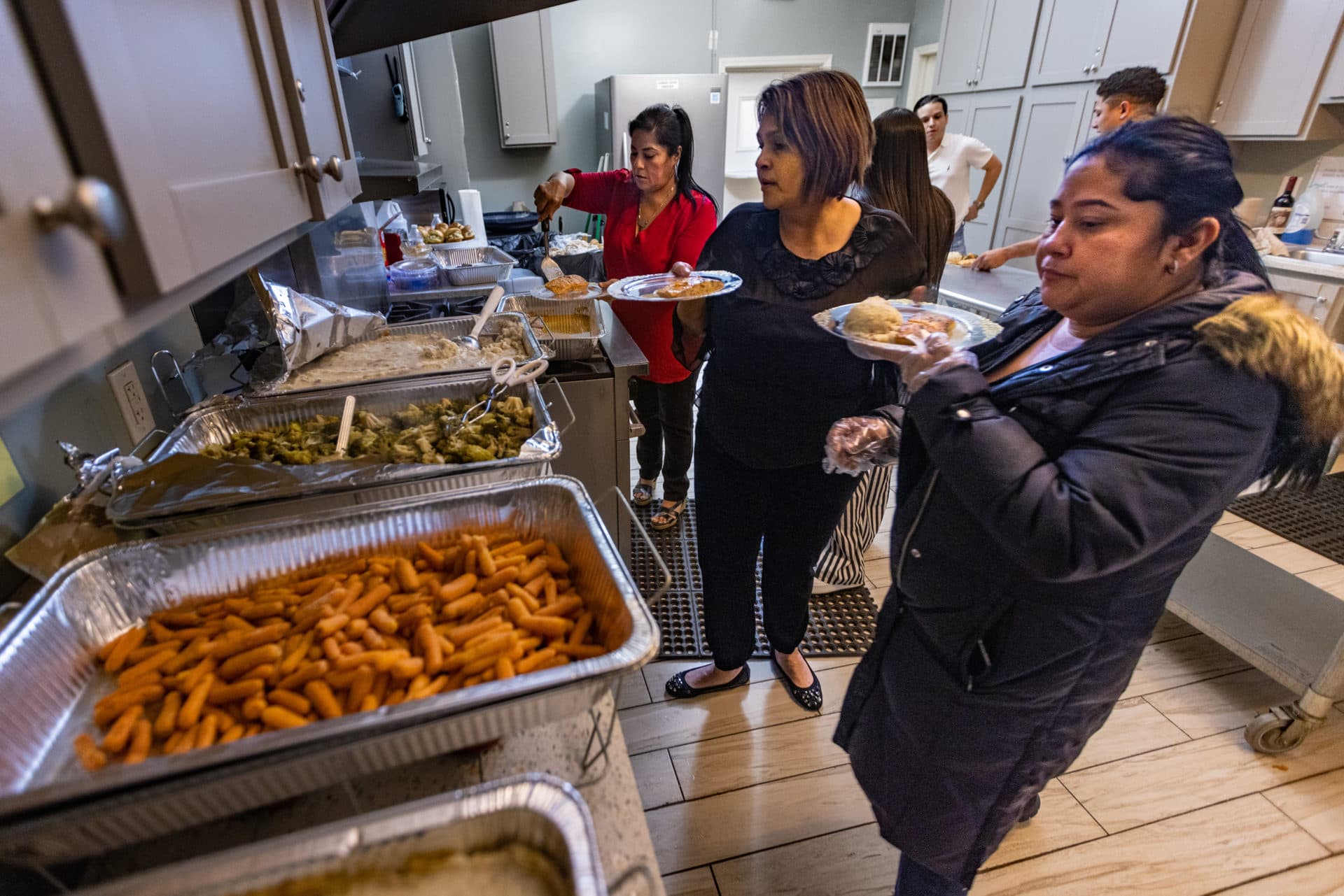 Isabel Rodriguez, center, and her cousins work to serve food for about 50 people at her mother's party. The 58-year-old prepared the food while balancing two jobs and helping her relatives. (Jesse Costa/WBUR)