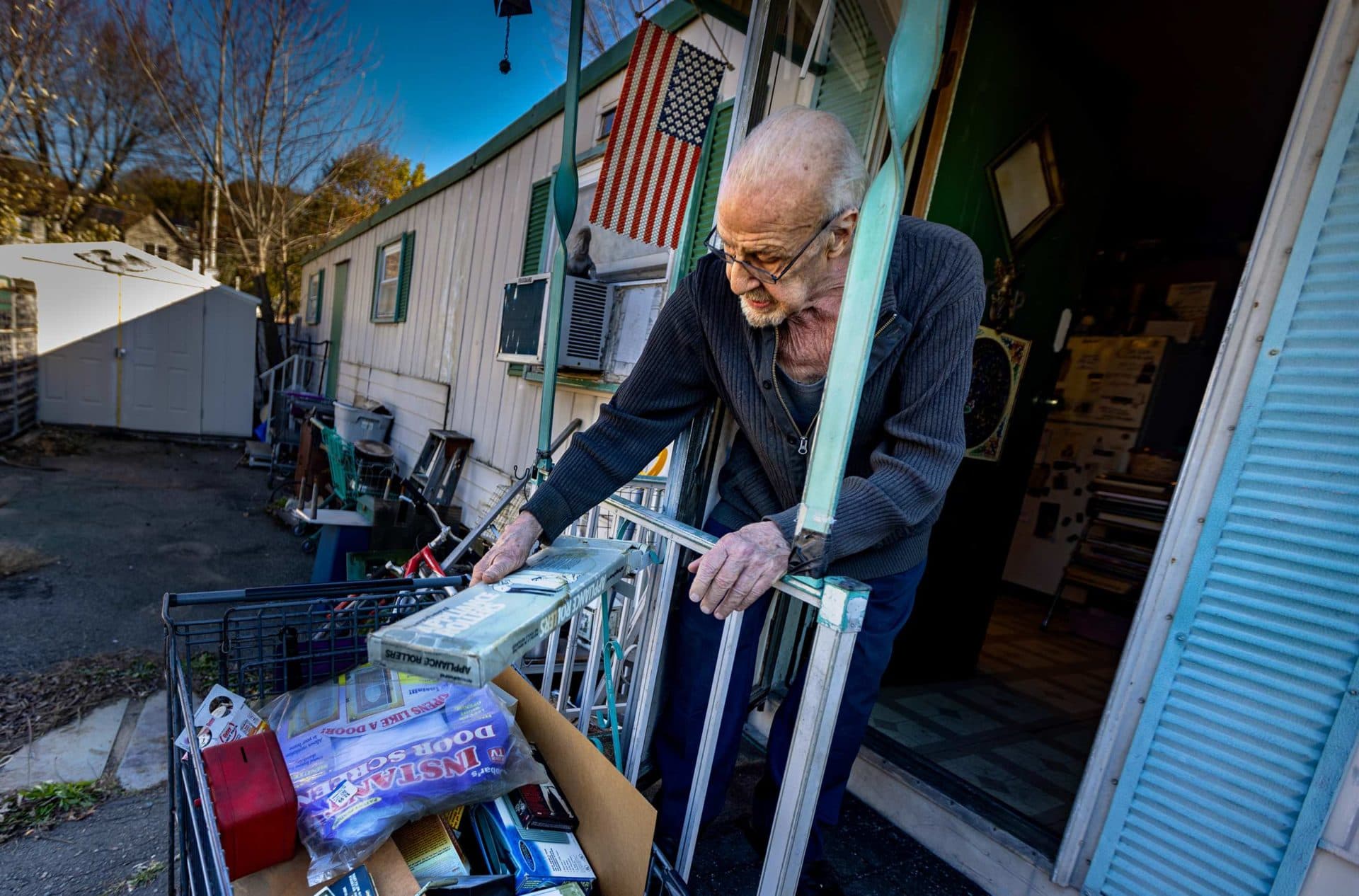 John Piazza places a box of appliance rollers into a shopping cart full of items to be thrown in the dumpster as he prepares to move out of his trailer in Revere. (Jesse Costa/WBUR)