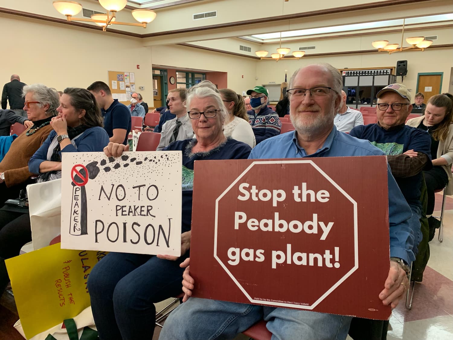 Susan and Ron Smoller hold signs at a Massachusetts Department of Environmental Protection hearing about the proposed Peabody &quot;peaker&quot; plant. (Courtesy of Mireille Bejjani)