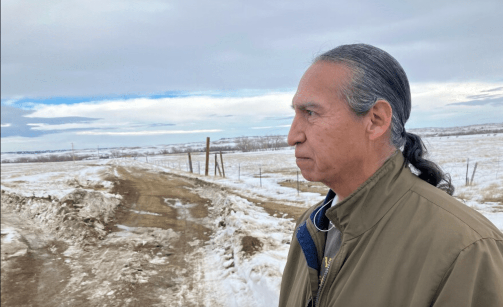 Michael He Crow, 60, stands on the road in Ogala, South Dakota that leads to the cabin where he grew up, on Dec. 27, 2022. (Nancy Eve Cohen/NEPM)