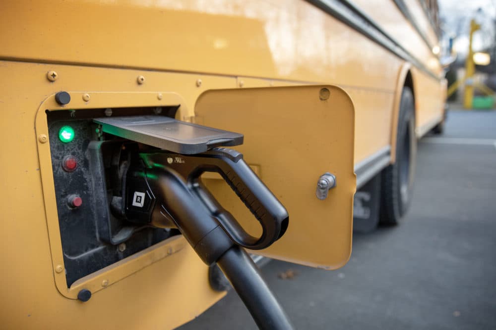 An electric school bus charging in its parking lot in Beverly, Mass. (Robin Lubbock/WBUR)