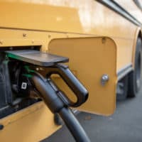 An electric school bus charging in its parking lot in Beverly, Mass. (Robin Lubbock/WBUR)
