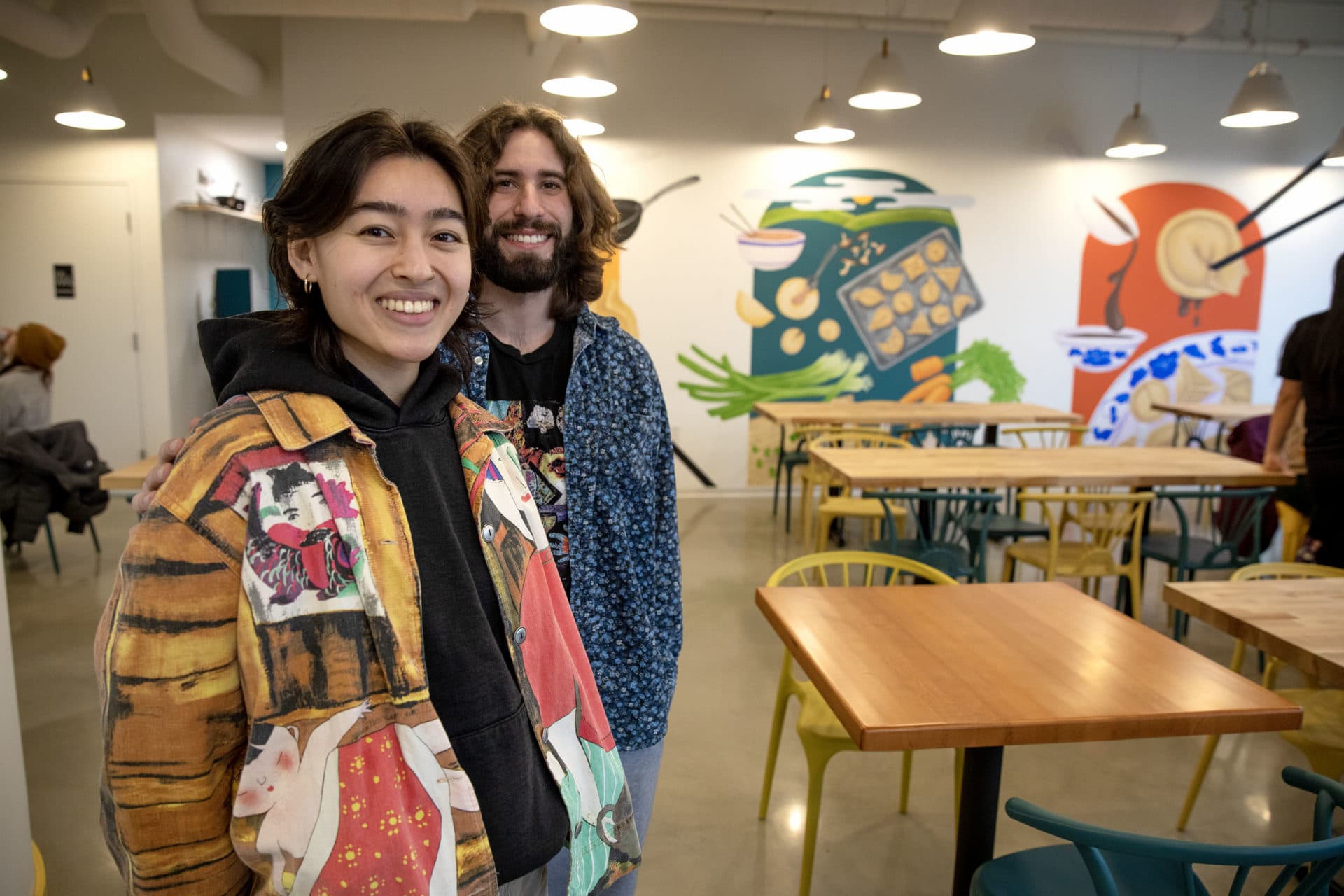Artist and designer Katelyn Lipton and muralist Sam Stubbs stand in the restaurant area of Mei Mei, with their murals on the wall behind them. (Robin Lubbock/WBUR)