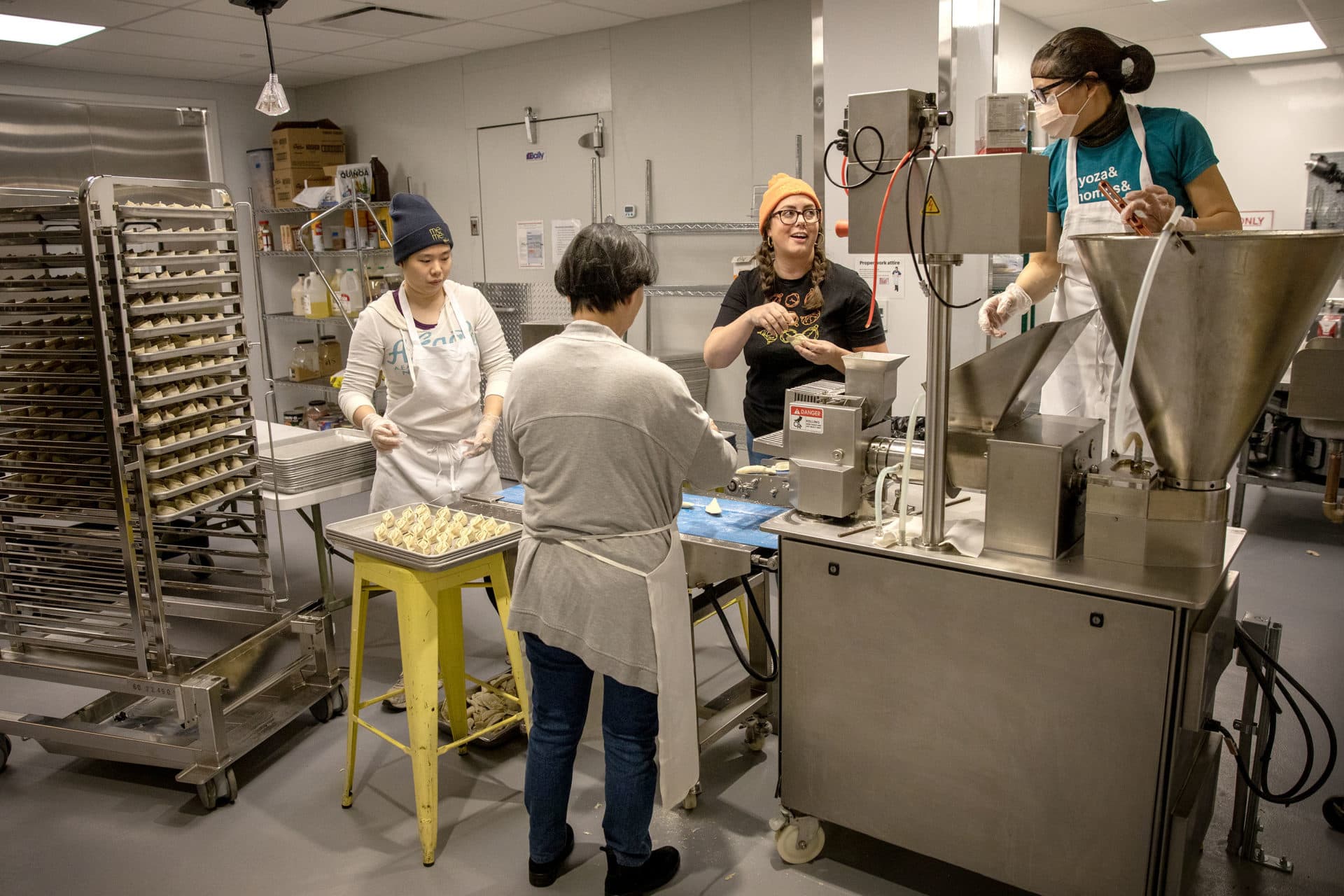 Mei Mei staff work together placing dumplings in trays as they roll off the machine. (Robin Lubbock/WBUR)