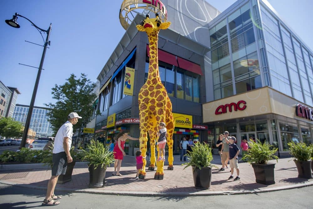 Children climb on Tessie the 20-foot-tall lego giraffe at Assembly Row in Somerville. (Jesse Costa/WBUR)