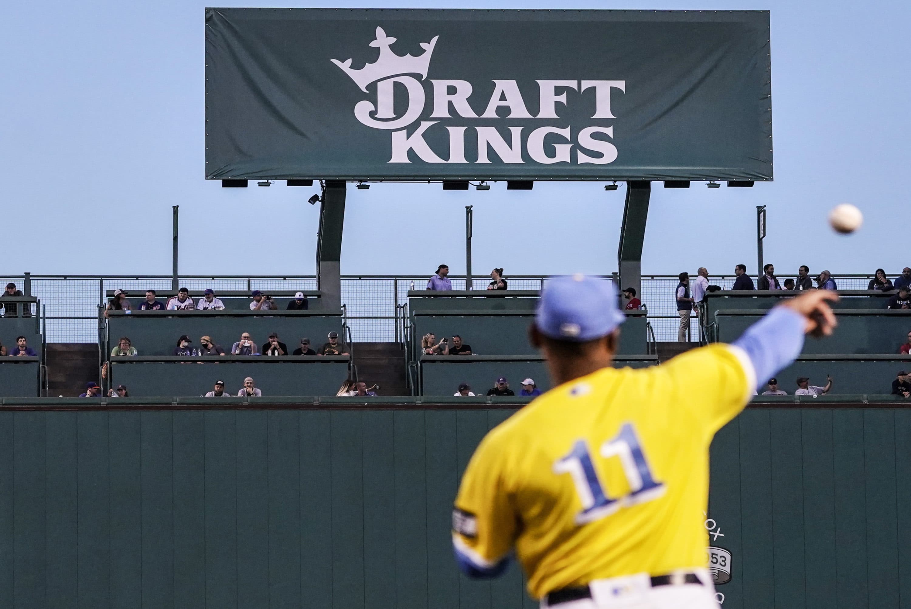 A left field scoreboard is covered under a DraftKings promotional as Boston Red Sox third baseman Rafael Devers (11) warms up before a baseball game at Fenway Park, Wednesday, Sept. 22, 2021, in Boston. (Charles Krupa/AP)