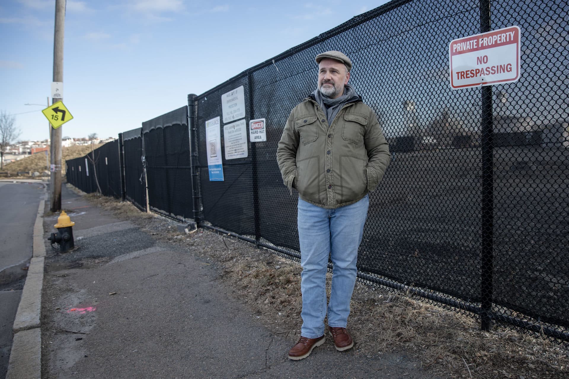 GreenRoots' Director of Waterfront and Climate Justice Initiatives John Walkey, stands by the fence at the site of the East Boston electrical substation. (Robin Lubbock/WBUR)