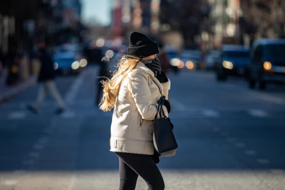 A woman covers her face from the bitter cold wind as she crosses Boylston Street in Copley Square. (Jesse Costa/WBUR)