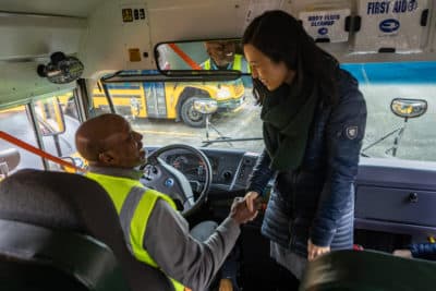 Jackson Janzier, a safety bus trainer, is greeted by Mayor Michelle Wu as she boards one of the city's new electric school buses. (Jesse Costa/WBUR)