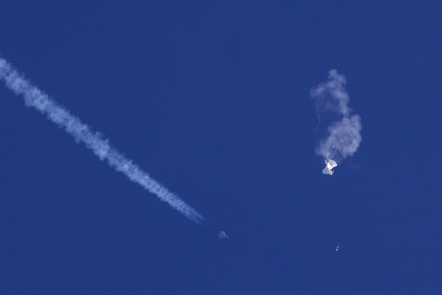 A fighter jet flies near the remnants of a large balloon after it was struck by a missile over the Atlantic Ocean, just off the coast of South Carolina near Myrtle Beach, Saturday, Feb. 4, 2023. The downing of the suspected Chinese spy balloon by a missile from an F-22 fighter jet created a spectacle over one of the state’s tourism hubs and drew crowds reacting with a mixture of bewildered gazing, distress and cheering. (Chad Fish via AP)