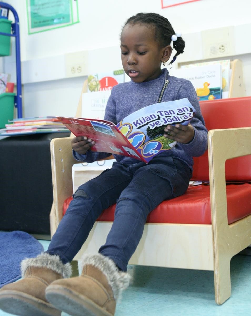 At the Mattahunt’s Toussaint L’Ouverture Academy, K-2 student Nheyseline Mentor, age 5, reads from the Haitian Kreyol book ‘Kijan Tan an ye Jodi a?’ (Seth Daniel/Dorchester Reporter)