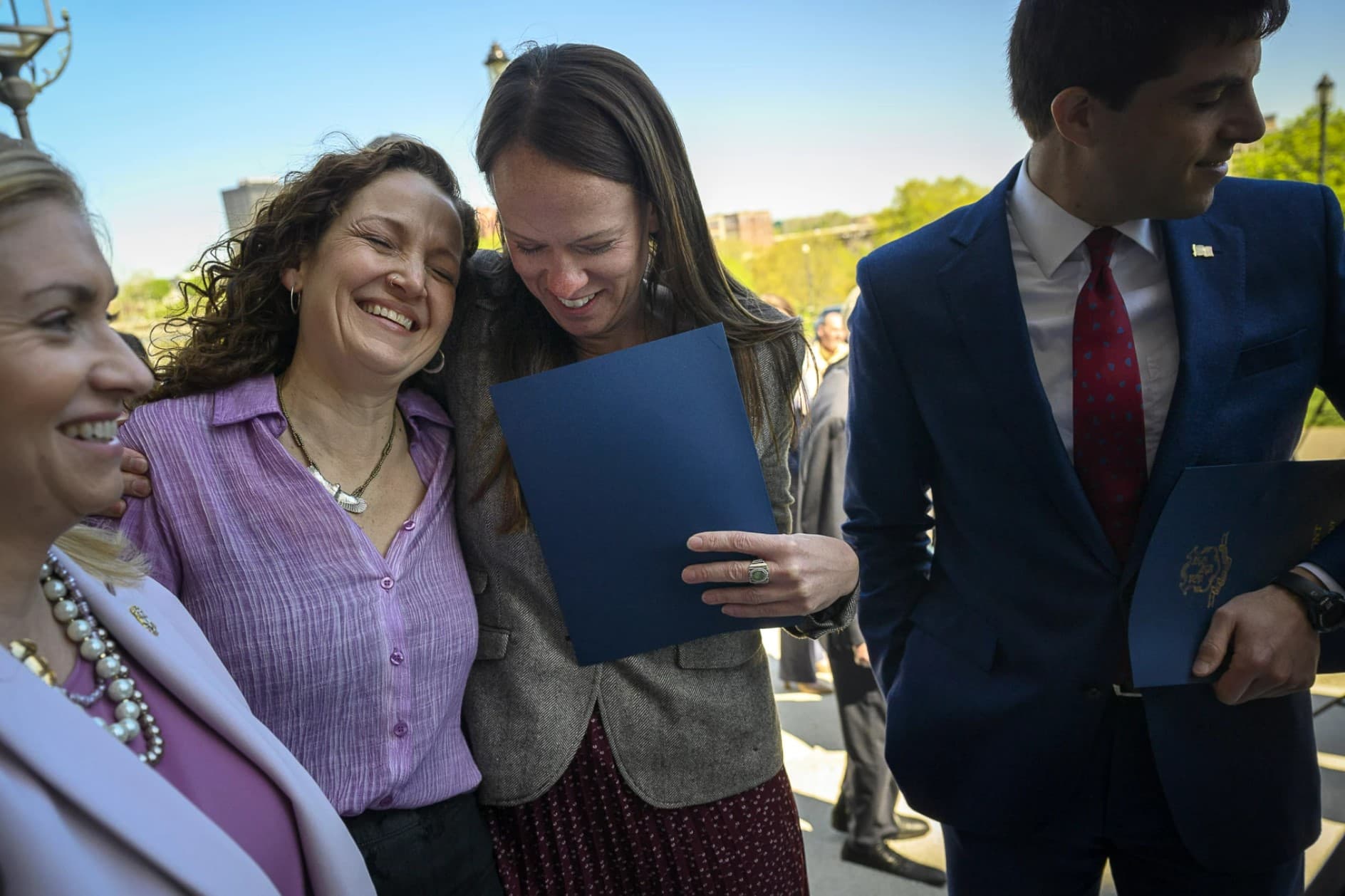 With state Rep. Matt Blumenthal (right), state Reps. Jillian Gilchrest (second from right) and Aimee Berger-Girvalo hug after a bill signing ceremony that extended legal protections to out-of-state health care providers and abortion patients. (Mark Mirko/Connecticut Public)