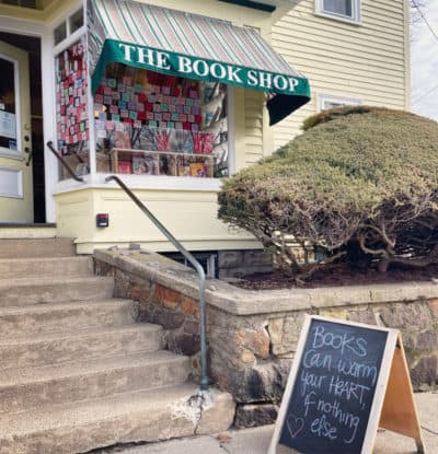 The author’s bookstore, post-its in the windows, and a sidewalk sign that says, “Books can warm your heart if nothing else.” Beverly, MA. 2023 (Courtesy Hannah Harlow)