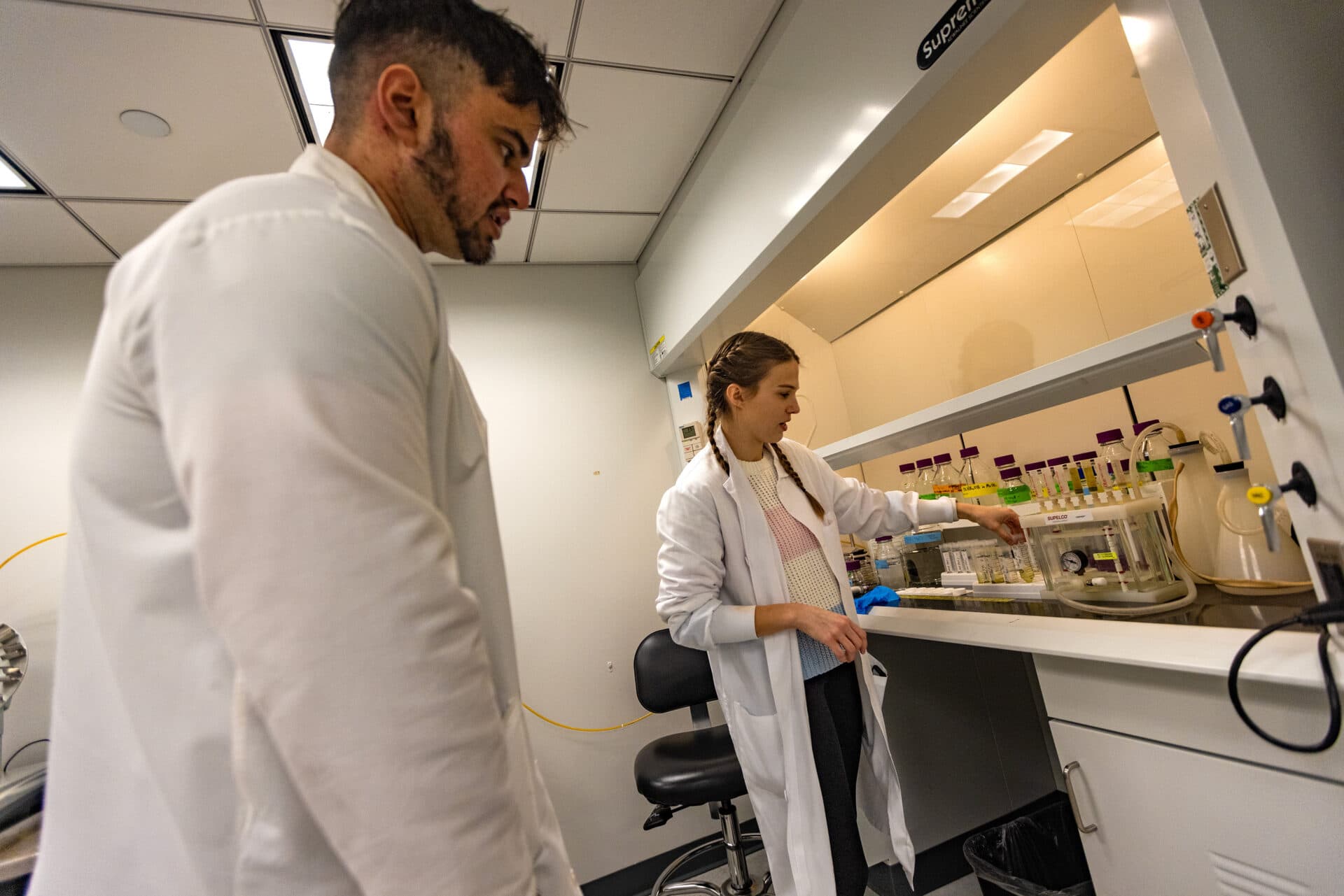 At a Harvard University lab, doctoral student Heidi Pickard, right, and research fellow Faiz Haque review the procedures to evaporate and separate PFAS chemical compounds from soil samples. (Jesse Costa/WBUR)
