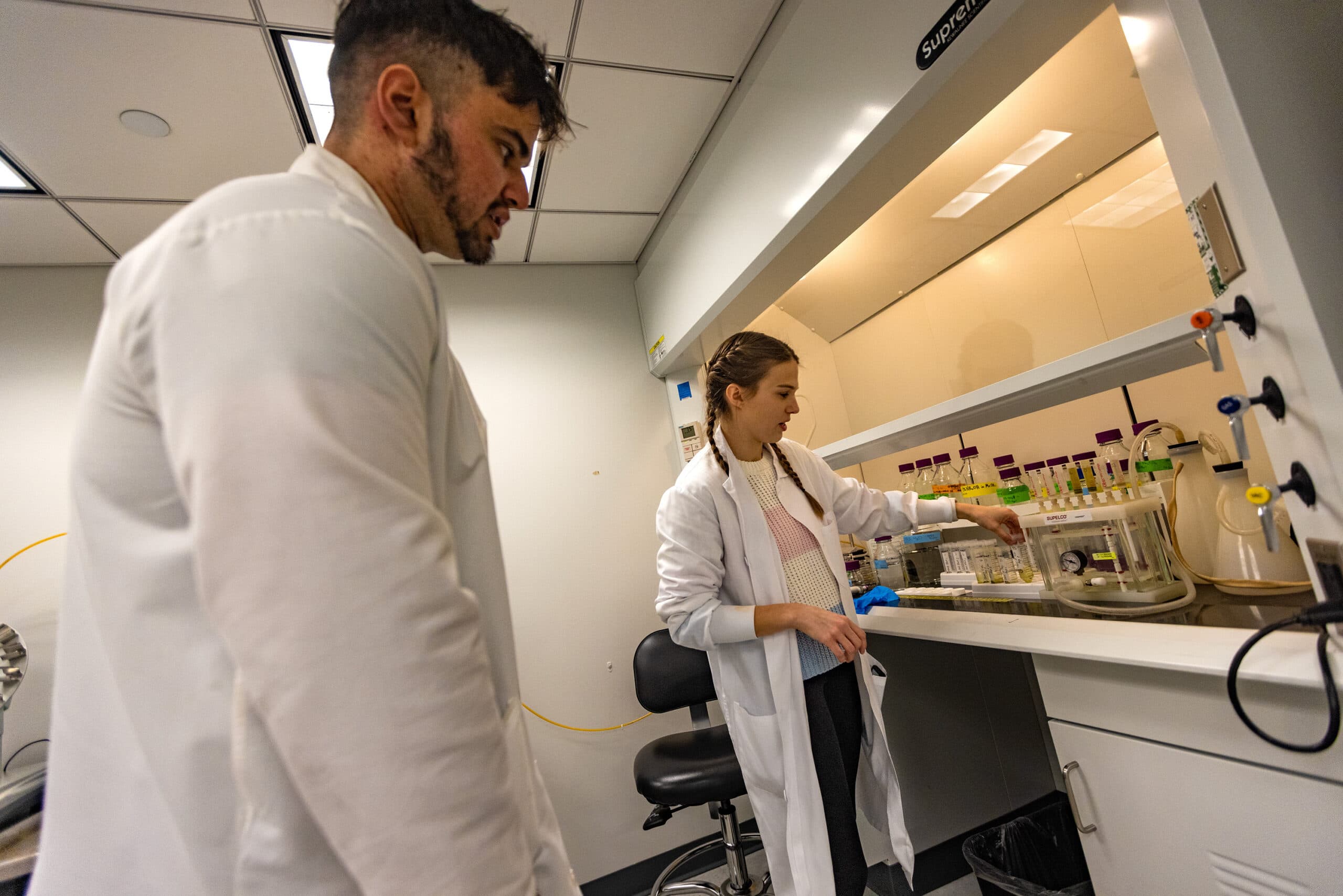 At a Harvard University lab, doctoral student Heidi Pickard, right, and research fellow Faiz Haque review the procedures to evaporate and separate PFAS chemical compounds from soil samples. (Jesse Costa/WBUR)