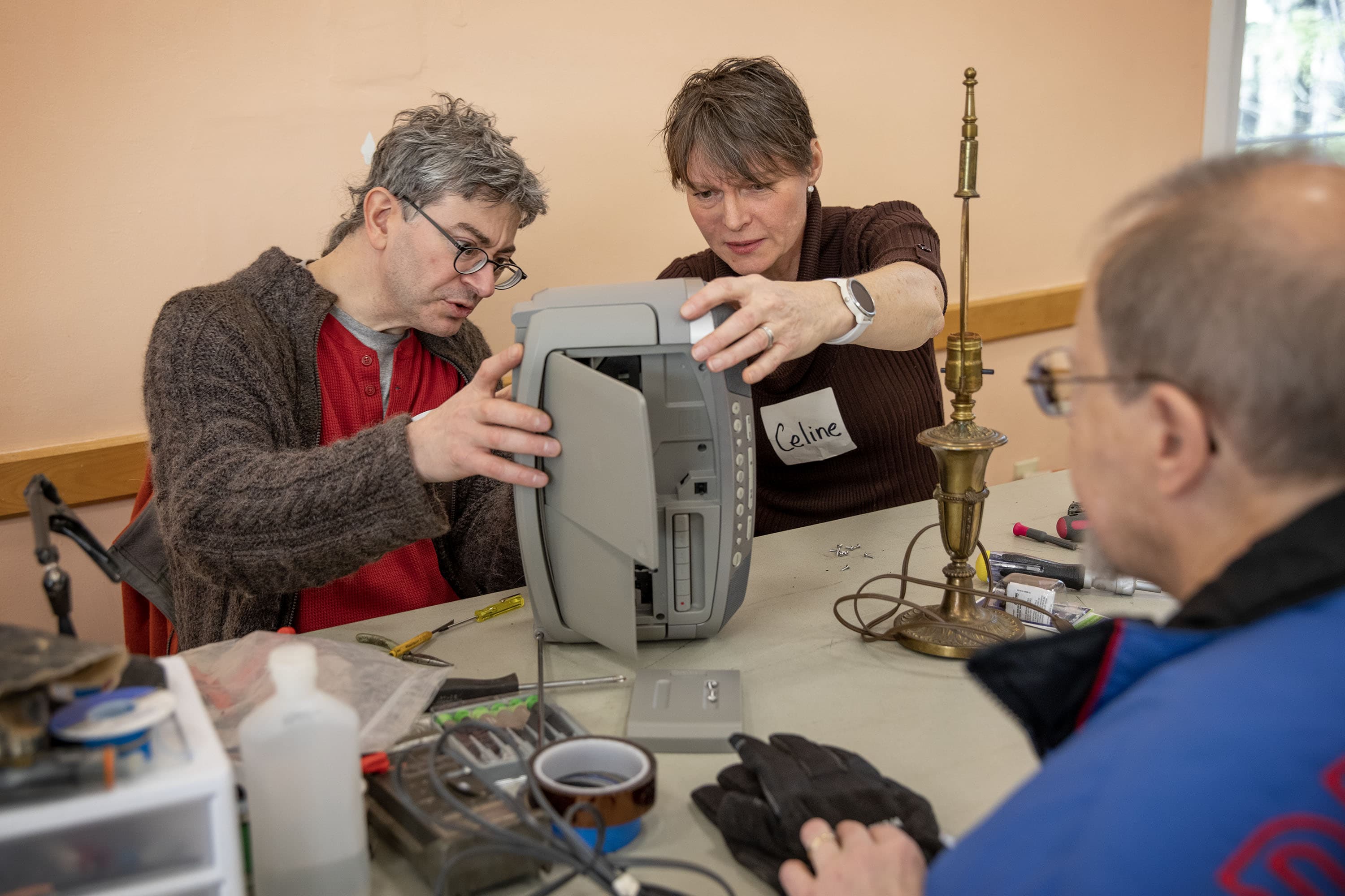 Celine Riard, right, and volunteer Ken Delpapa, left, examine Peter Stassa's CD/cassette player at Framingham's Repair Cafe. (Robin Lubbock/WBUR)
