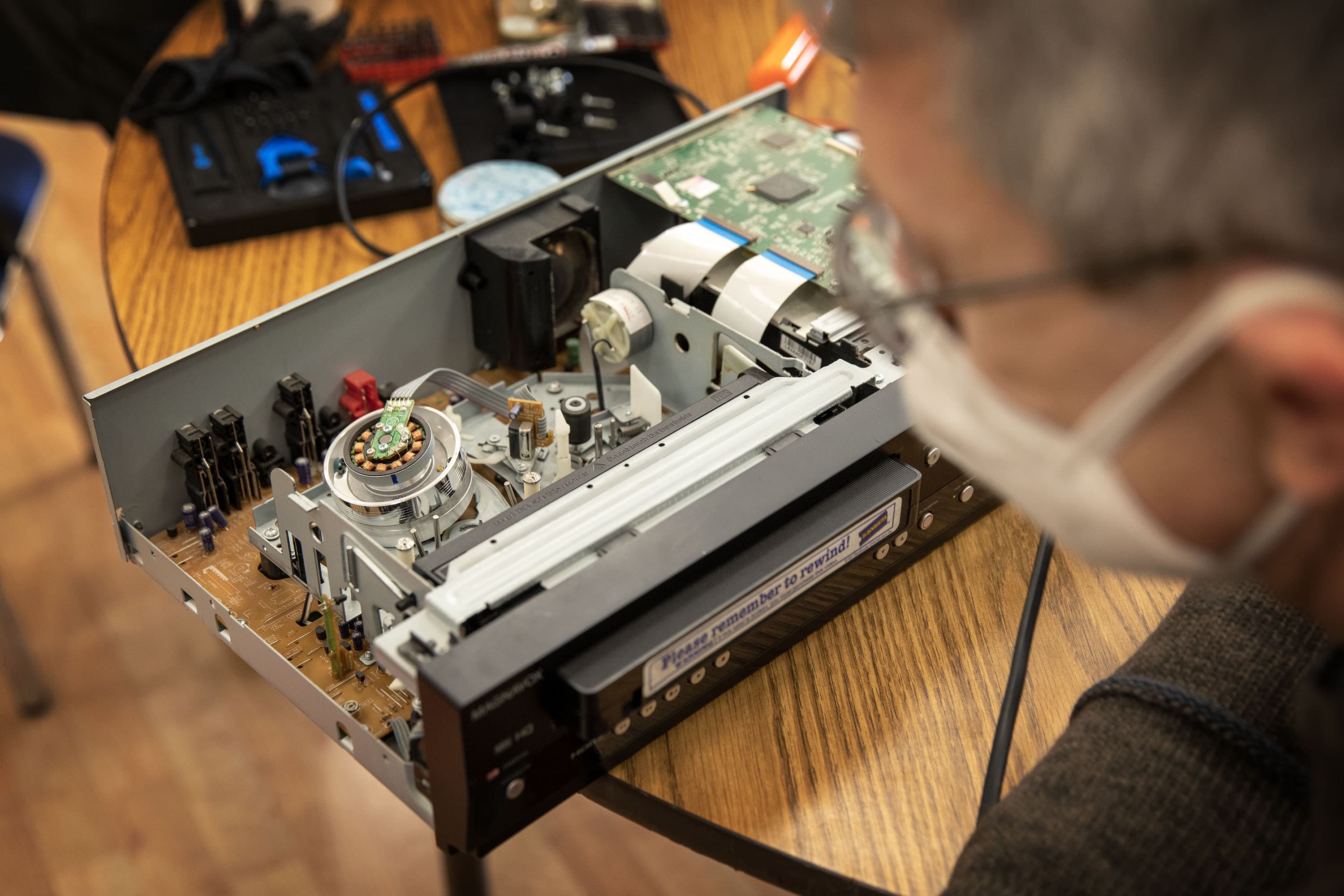 On the electronics table at the Repair Cafe, Justin Goding examines the inside of VHS video cassette machine. (Robin Lubbock/WBUR)