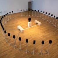 Artist Jace Clayton stands in the center of “40 Part Part,” an interactive installation that requires the visitor to connect their smartphone, laptop, or tablet. The artist’s complex processing algorithm alters the participant’s audio in unexpected ways and is heard through the forty speakers surrounding them. (Jesse Costa/WBUR)