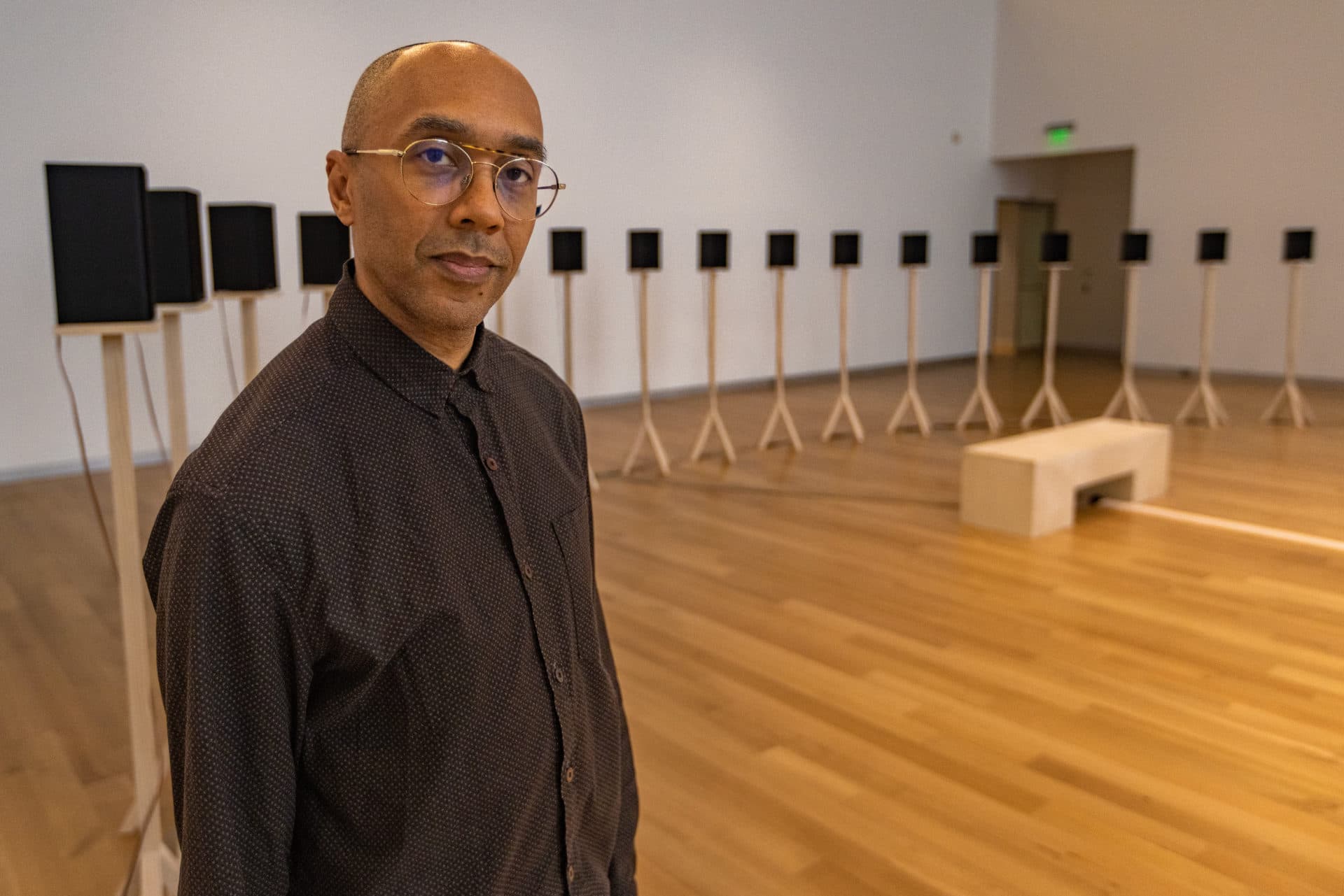 Artist Jace Clayton stands in front of a line of speakers, part of his show “They Are Part” at the MAAM. (Jesse Costa/WBUR)