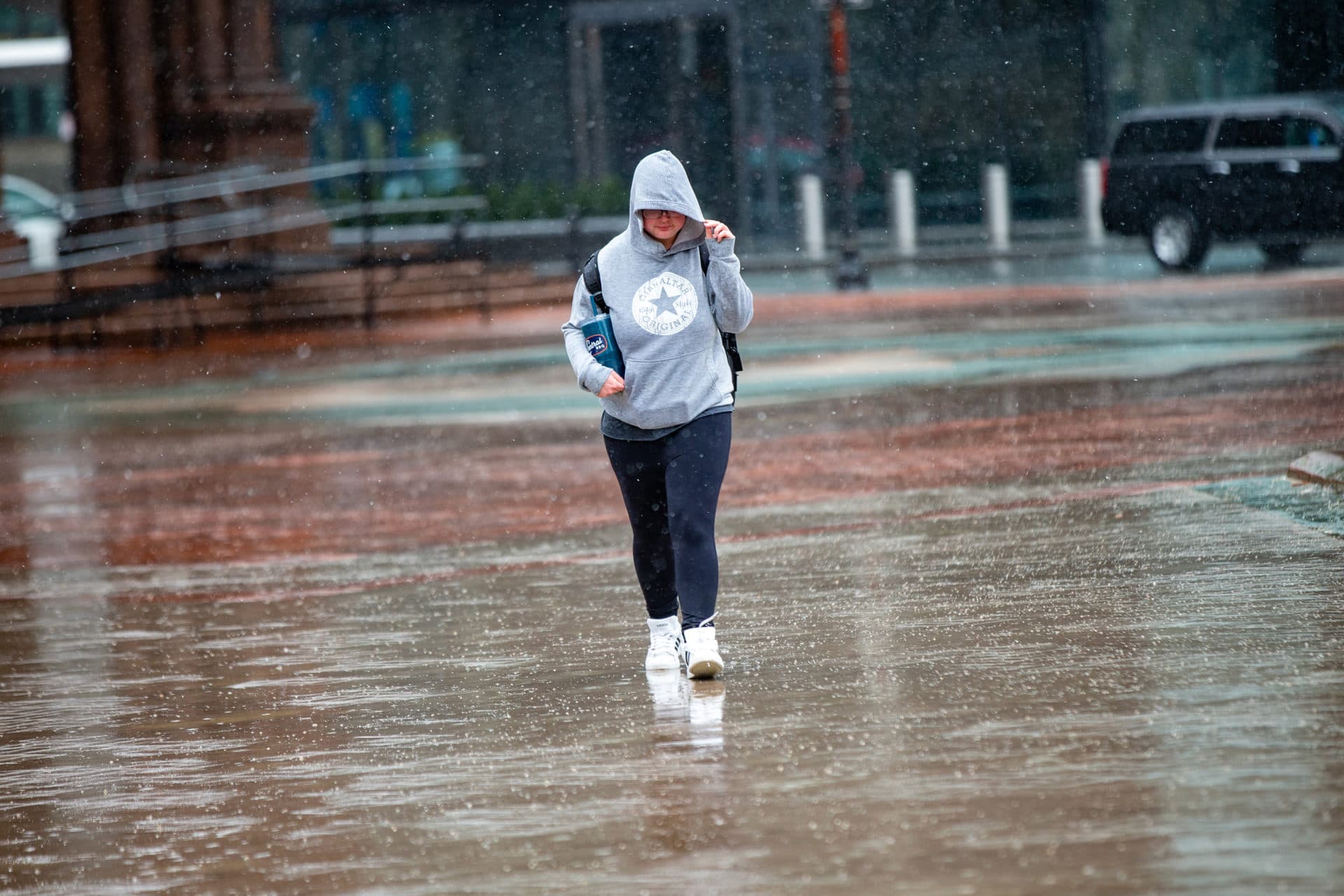 A woman holds her hood down against the storm's fierce and wet winds as she walks in Copley Square. (Jesse Costa/WBUR)