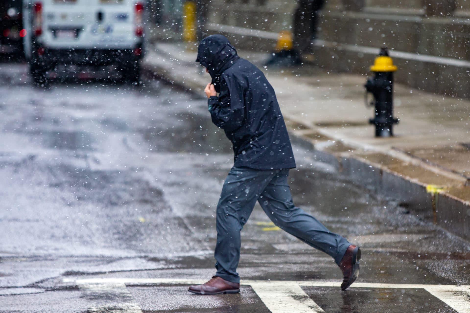 A man holds his hood down walking into the wind down St. James Avenue in the windy wintery mix of rain and snow. (Jesse Costa/WBUR)