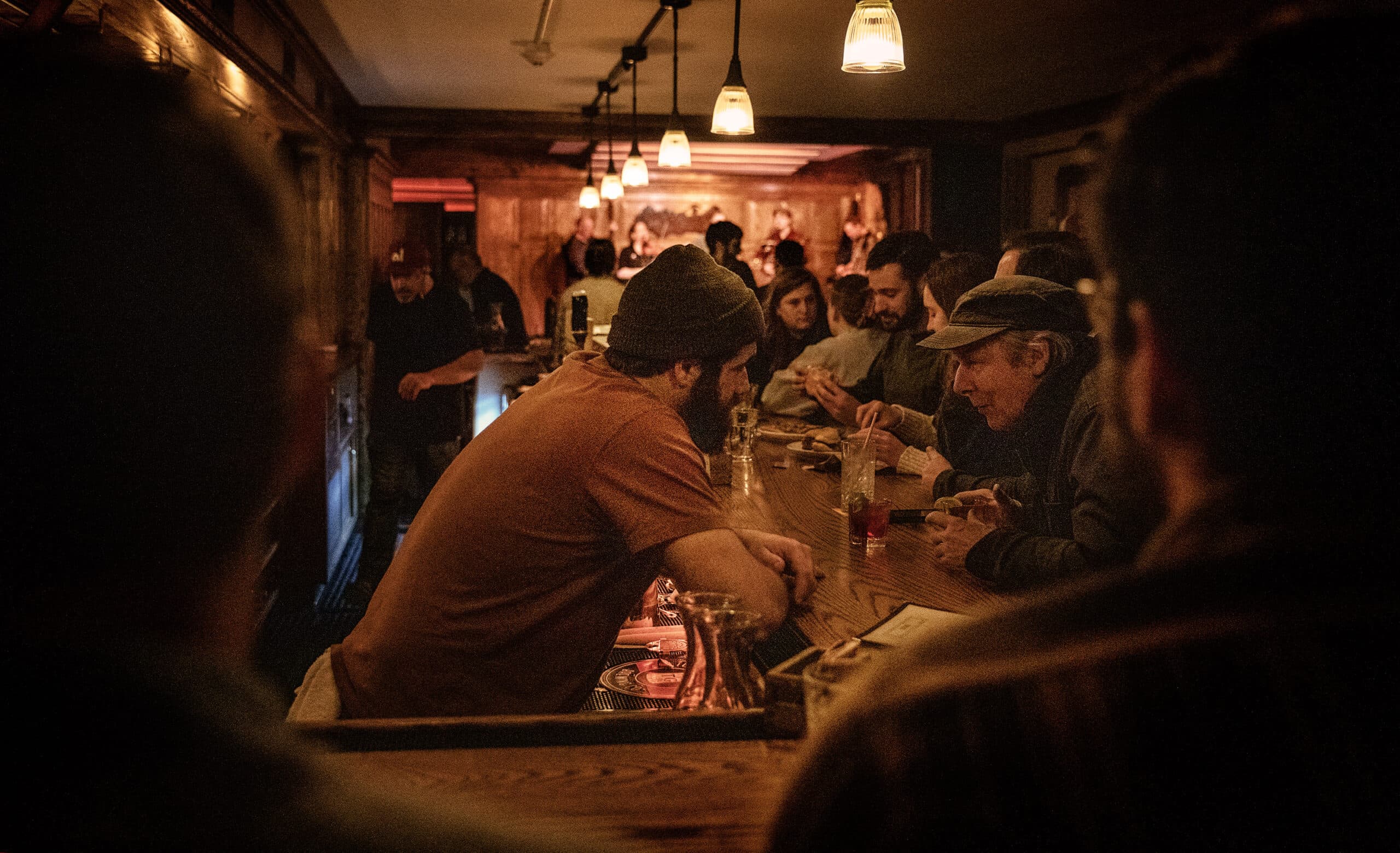 Manager Alexander Sirigu talks with a customer at the long bar of Atwoods, as the band plays on the stage at the far end of room. (Robin Lubbock/WBUR)