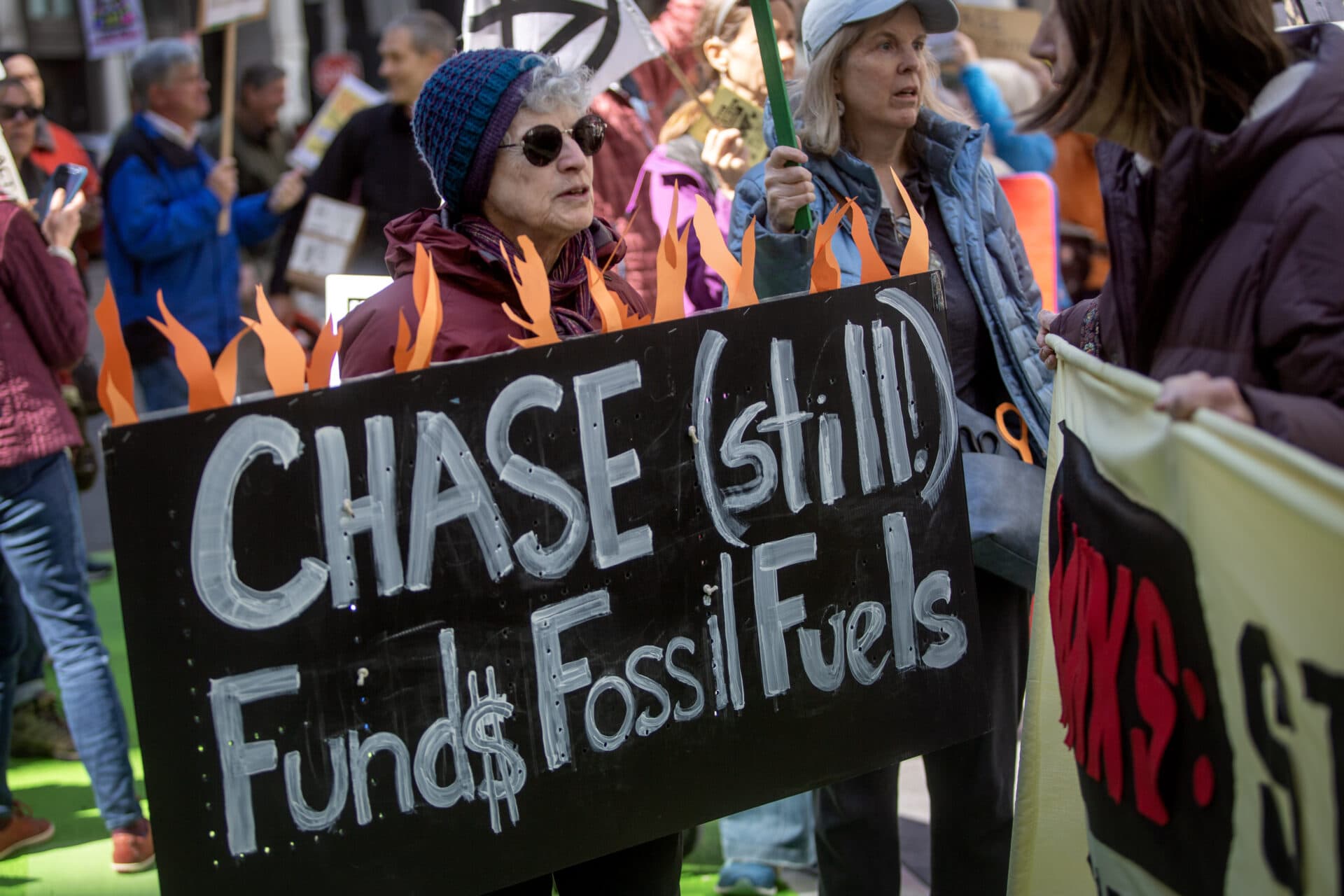 Boston protesters carry signs calling on banks to stop funding fossil fuel projects. (Credit: Robin Lubbock/WBUR)