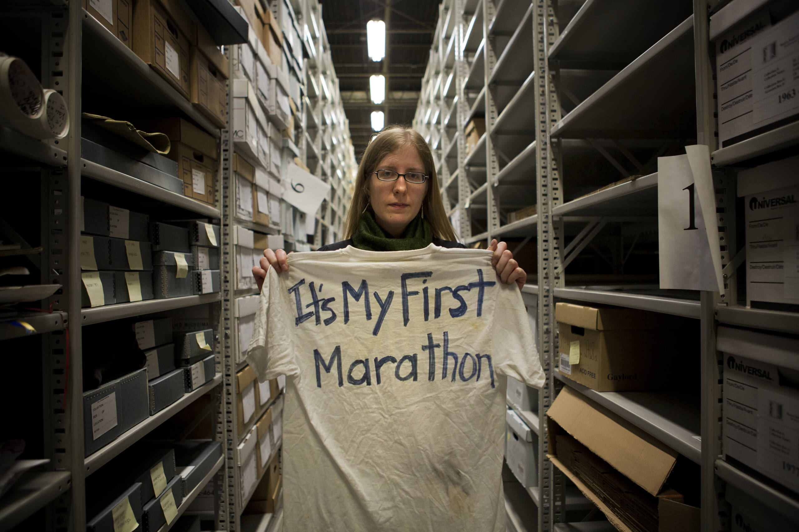 City archivist Marta Crilly holds a "It's My First Marathon" t-shirt inside a cavernous, temperature-controlled warehouse in West Roxbury holding dozens of boxes on its towering shelves that contain items from a makeshift memorial at Copley Square after the bombings. (Jesse Costa/WBUR)