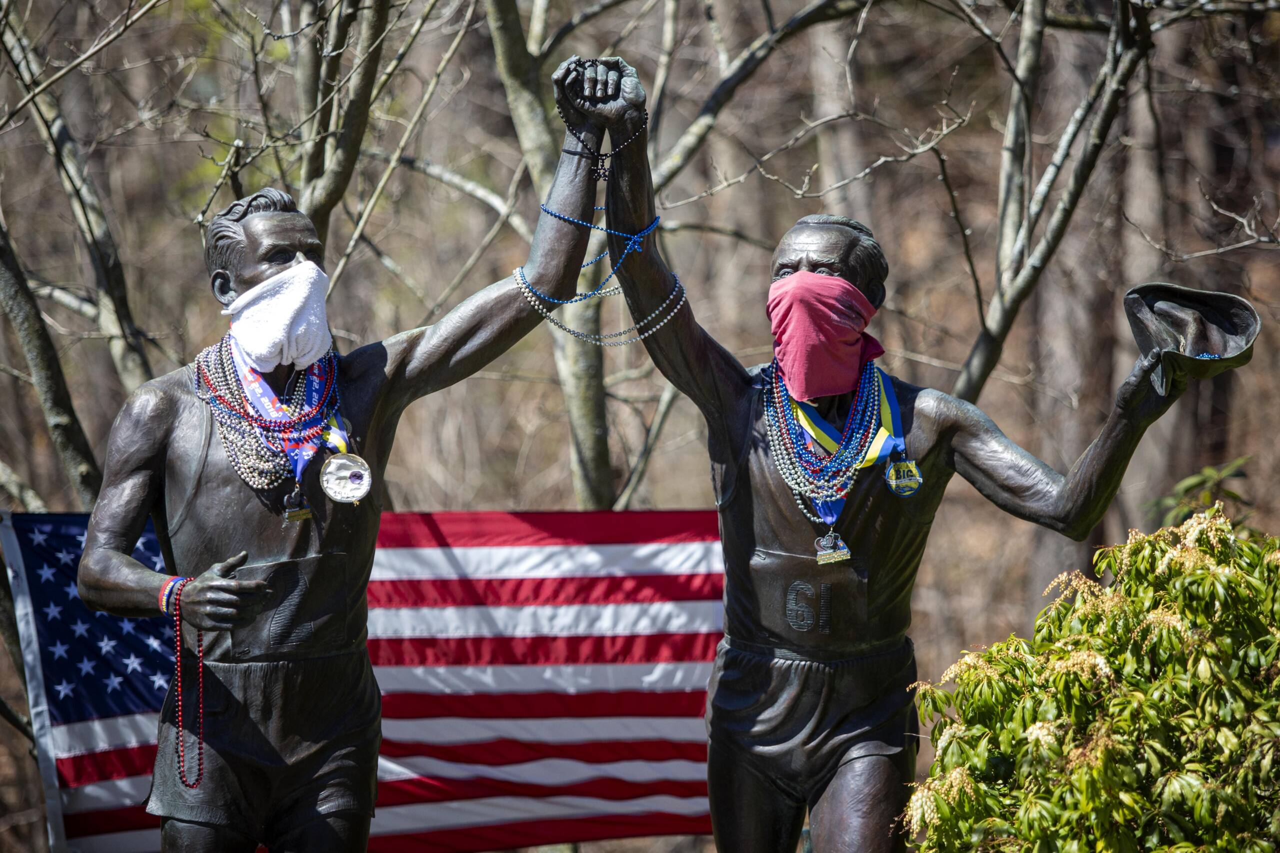 The two versions of marathon runner Johnny Kelley, aged 27 and 84, wear masks at the "Young at Heart" sculpture on Commonwealth Avenue in Newton. (Robin Lubbock/WBUR)