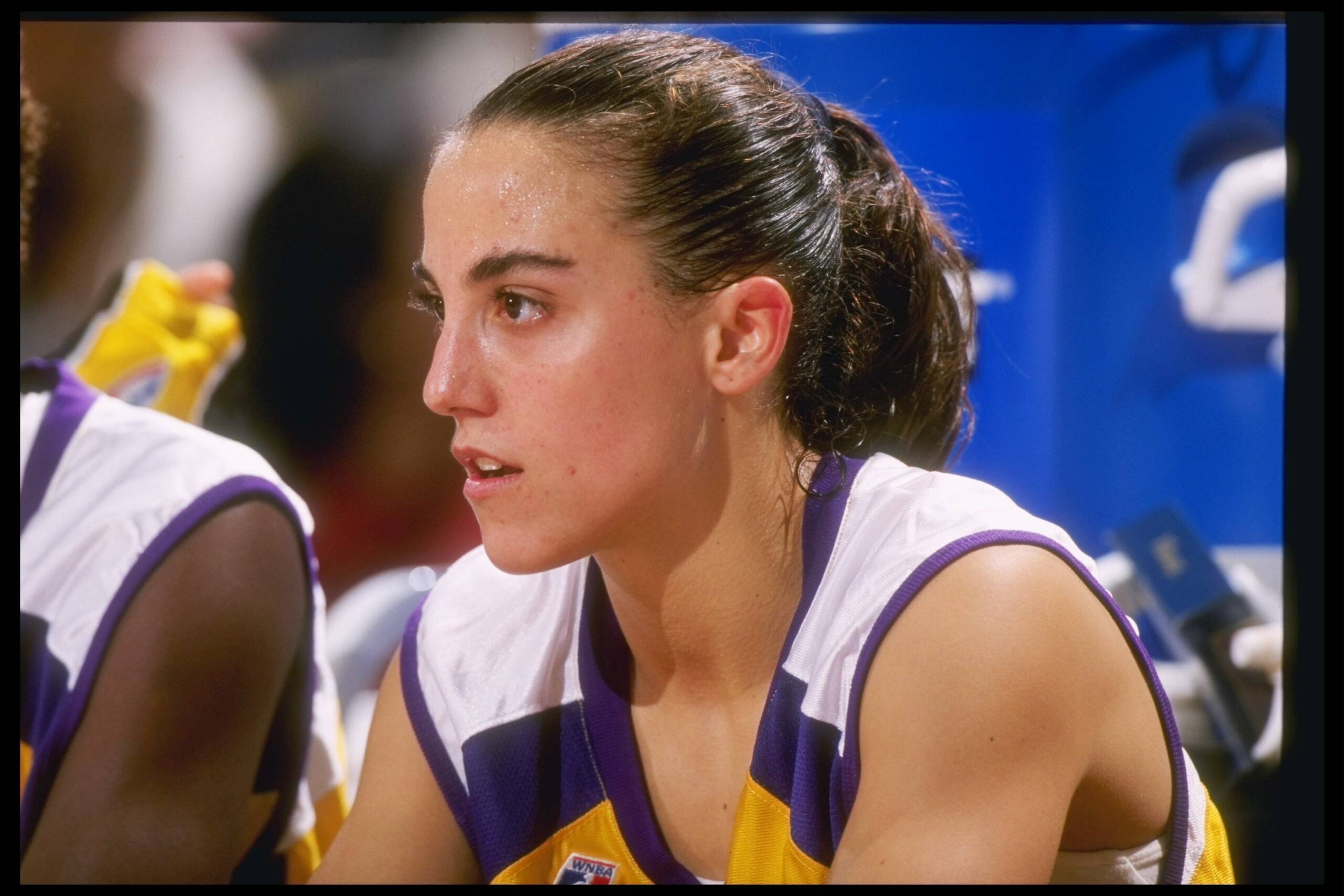 A woman with medium skin tone sitting in a basketball uniform. 