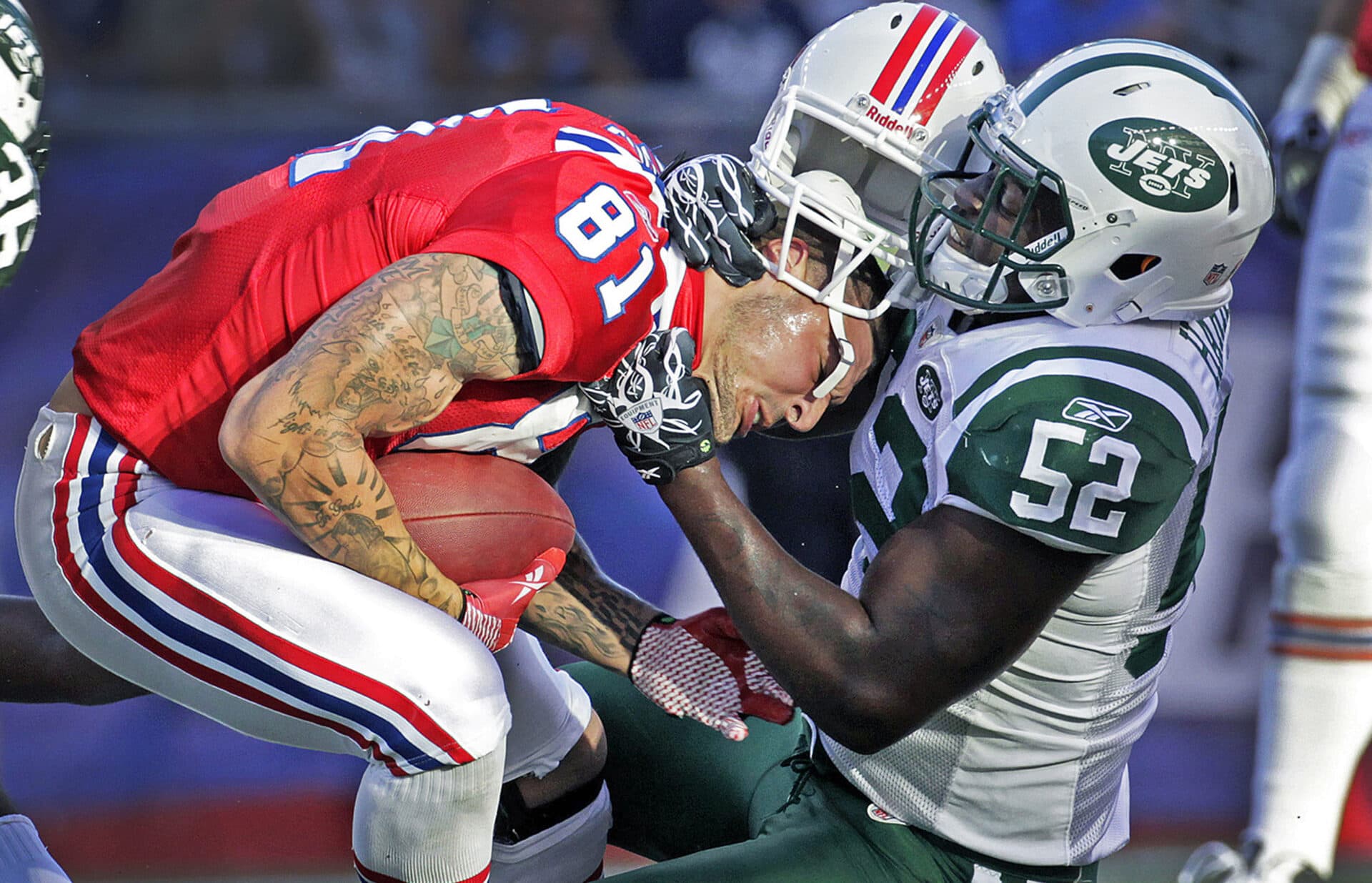 In this 2011 Boston Globe file photo, Patriots tight end Aaron Hernandez, left, is taken down by a Jets player after a catch and loses his helmet in the process. (Jim Davis/Boston Globe)