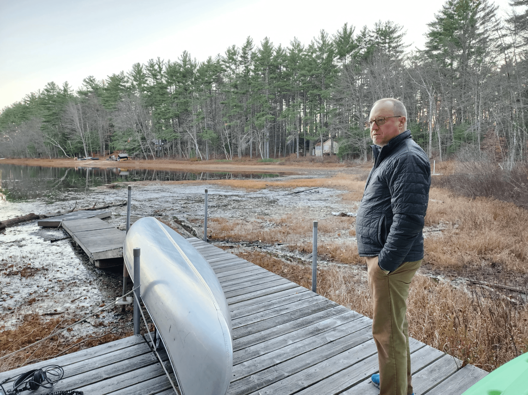 Jim Metivier stands next to the canoe on his dock on Long Pond in Denmark, Maine, in Nov. 2022. Susan Sharon/Maine Public)