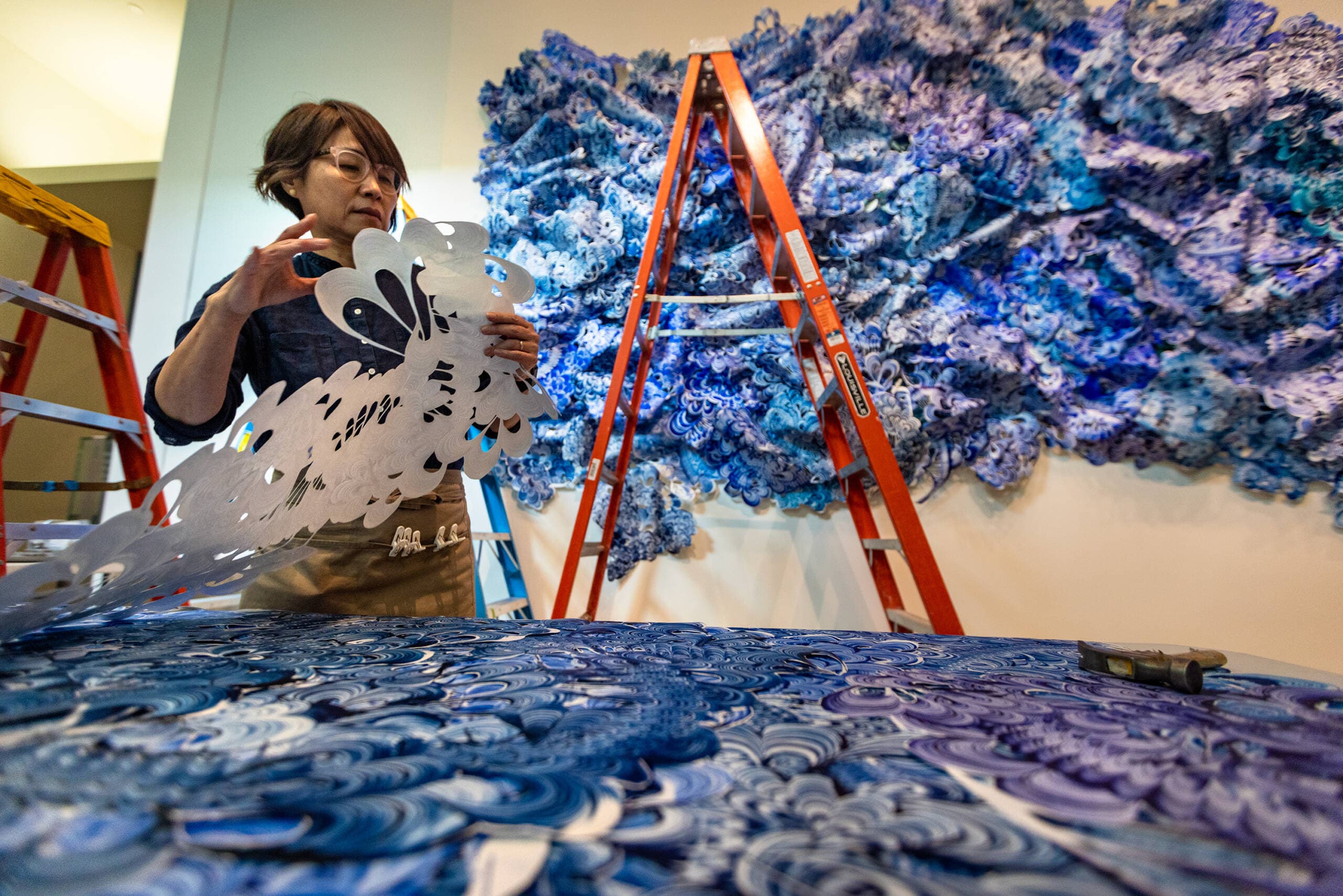 Taiko Chandler picks up a piece of Tyvek as she installs her piece “Blue Surge,” showing as part of the exhibition "Hokusai: Inspiration and Influence" at the Museum of Fine Arts, Boston. (Jesse Costa/WBUR)