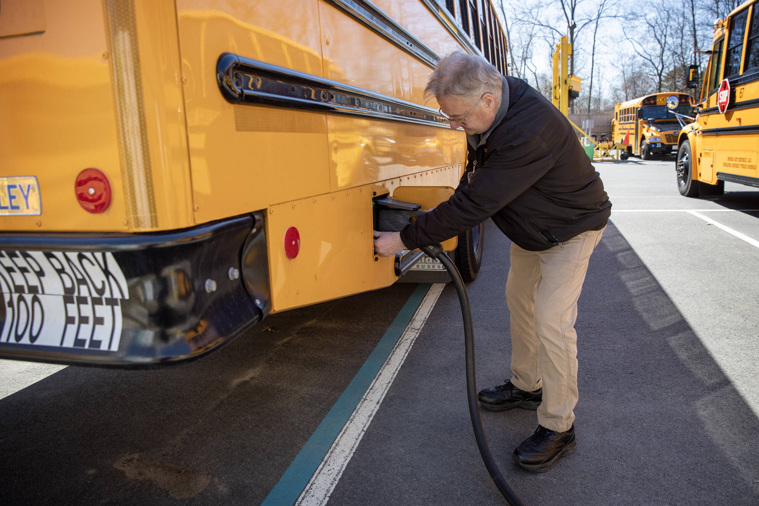 District Transportation Director Dana Cruickshank unplugs the charging cable from one of Beverly's electric school buses. (Robin Lubbock/WBUR)