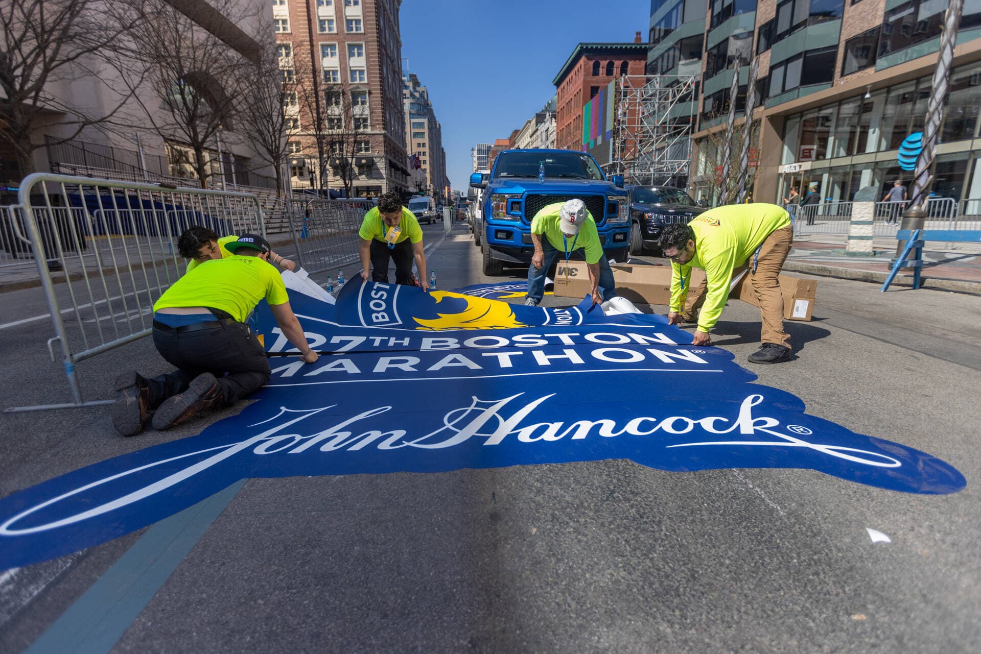 On Boylston Street, workers lay down a decal with the sponsor John Hancock's logo ahead of the 127th Boston Marathon. (Jesse Costa/WBUR)