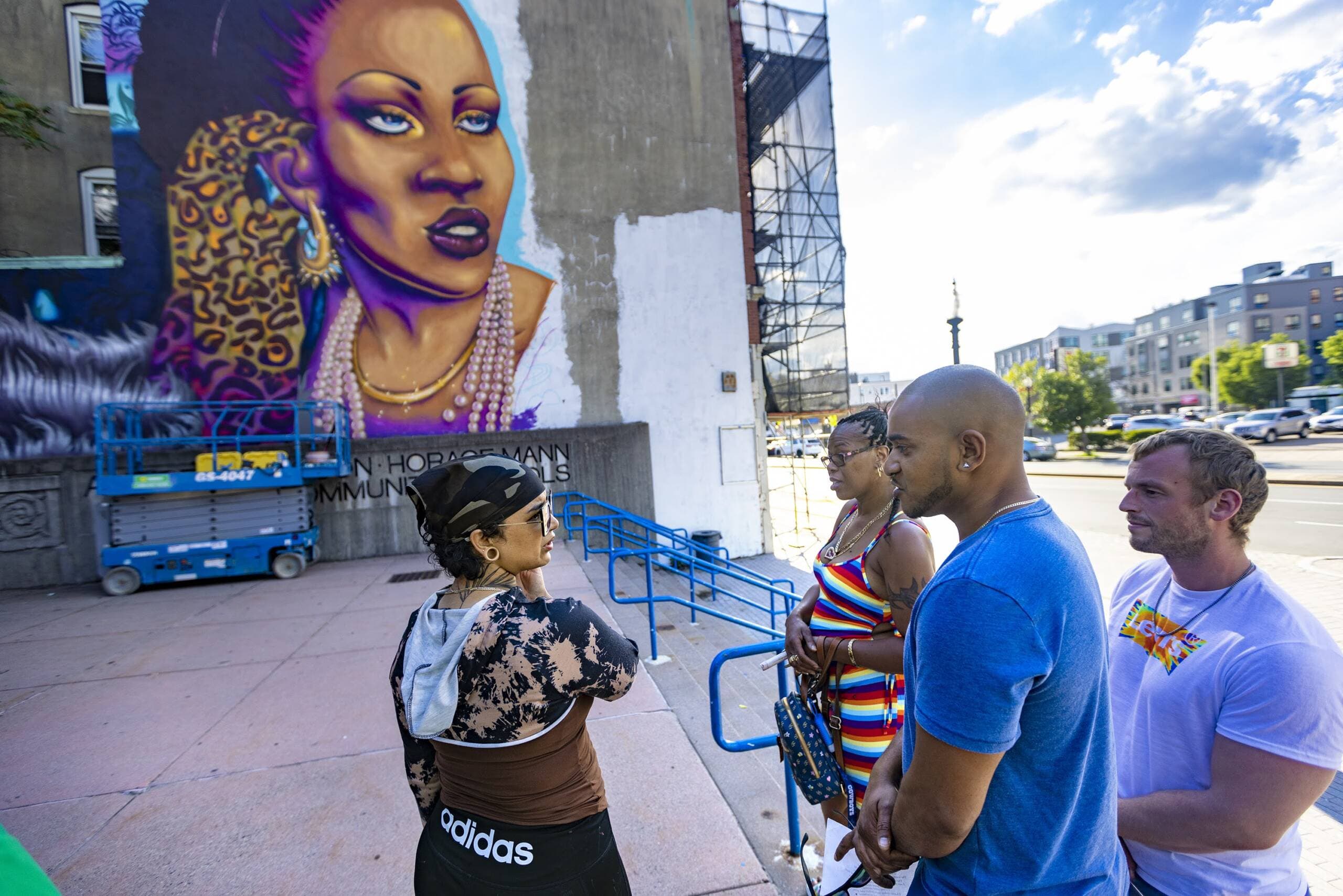 Taufiq Chowdhury and Kim Hester speak with artist Rixy in front of the Allston mural "Rita's Spotlight," honoring the memory of Rita Hester. Street Theory helped install this mural in the neighborhood. (Jesse Costa/WBUR)