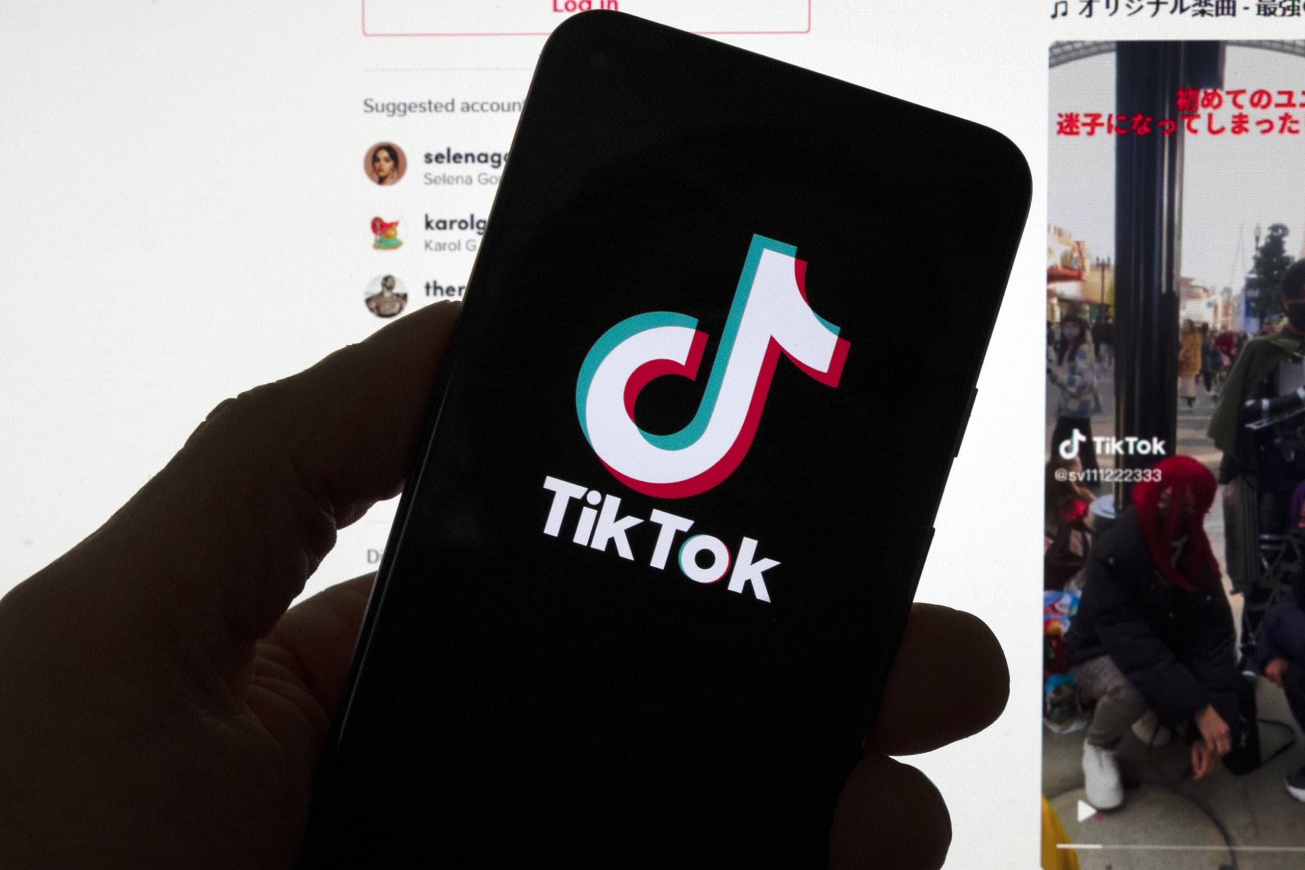 The TikTok logo is seen on a mobile phone in front of a computer screen which displays the TikTok home screen. (Michael Dwyer/AP)