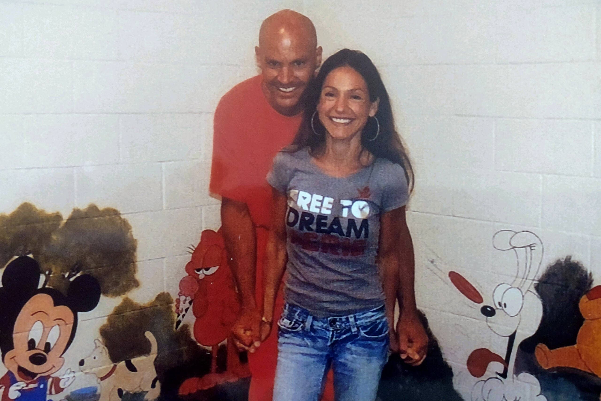 Jacob Wideman, a multiracial man in a prison uniform, with Marta DeSoto, a Spanish woman. Cartoon characters are painted on the wall. 