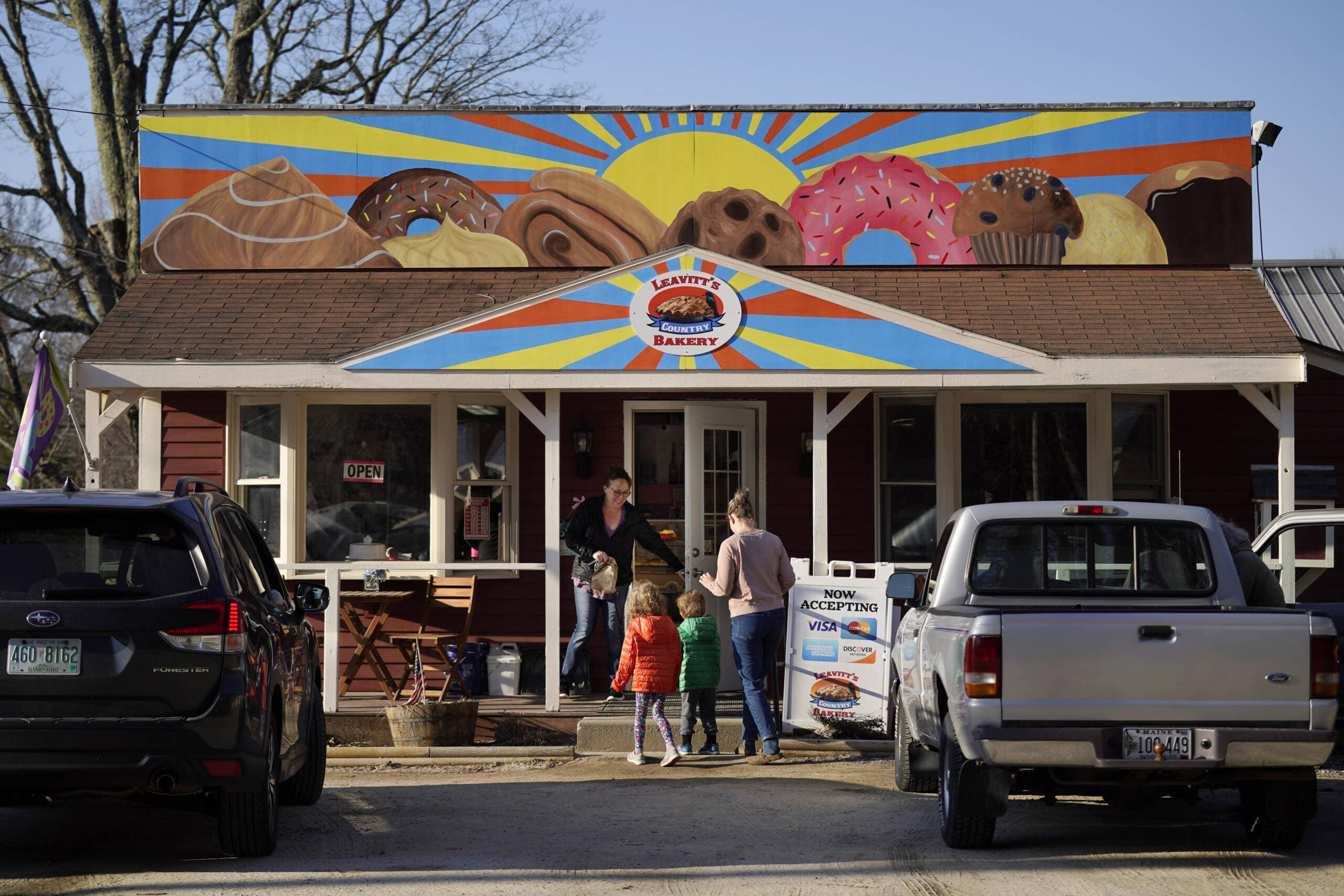 A customer holds the door for a family arriving at Leavitt's Country Bakery, April 13, in Conway, N.H. The large painting of pastries created by students and displayed over the bakery is at the center of a legal battle pitting a zoning ordinance against freedom-of-speech rights. (Robert F. Bukaty/AP)