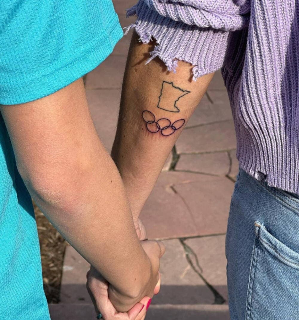 The Olympic rings and Minnesota tattoos on Kara Goucher's arm, as she holds her son, Colt's, hand in March 2023. (Courtesy Kara Goucher via Instagram)