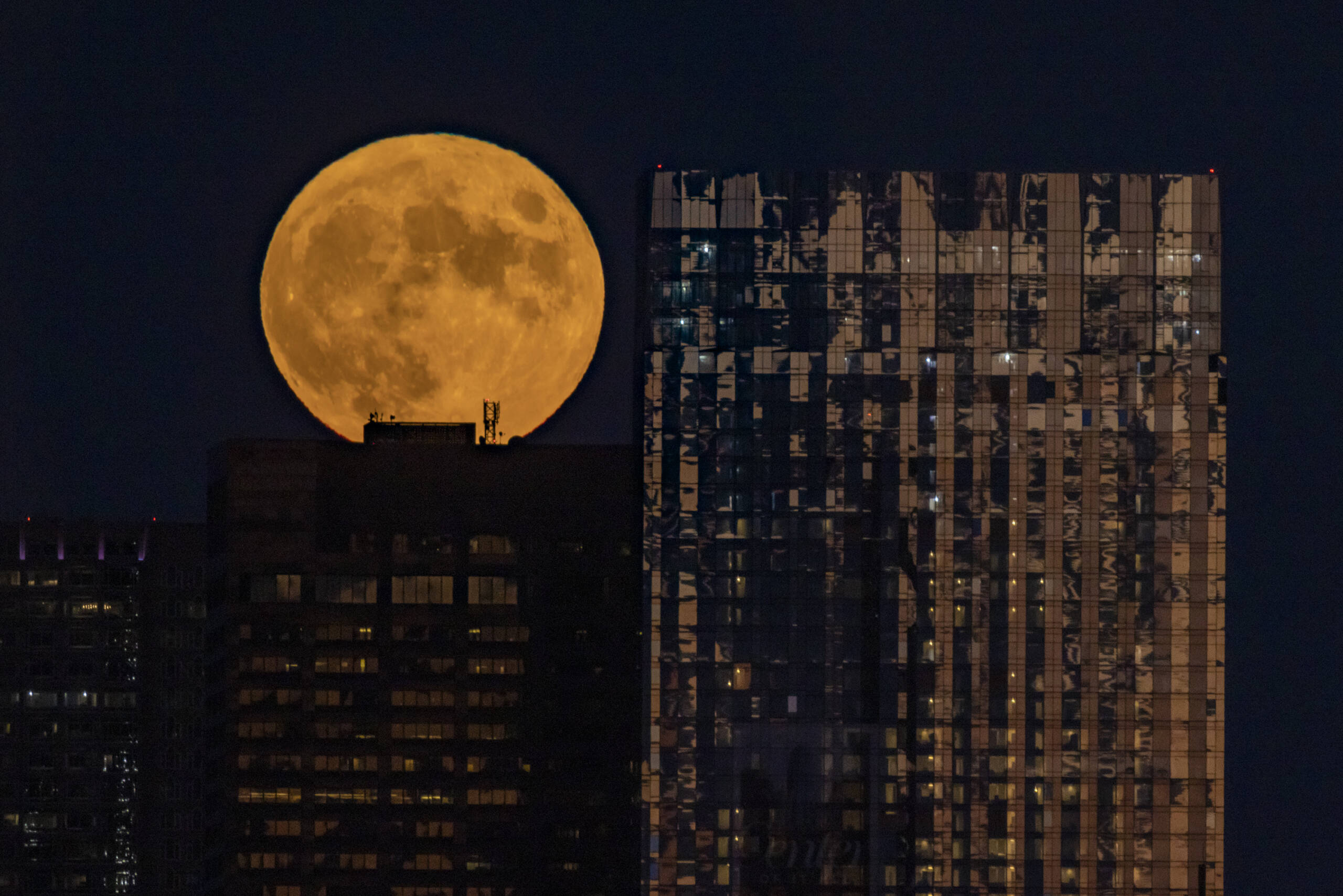 Boston skyscrapers are silhouetted against a full moon. (WBUR)