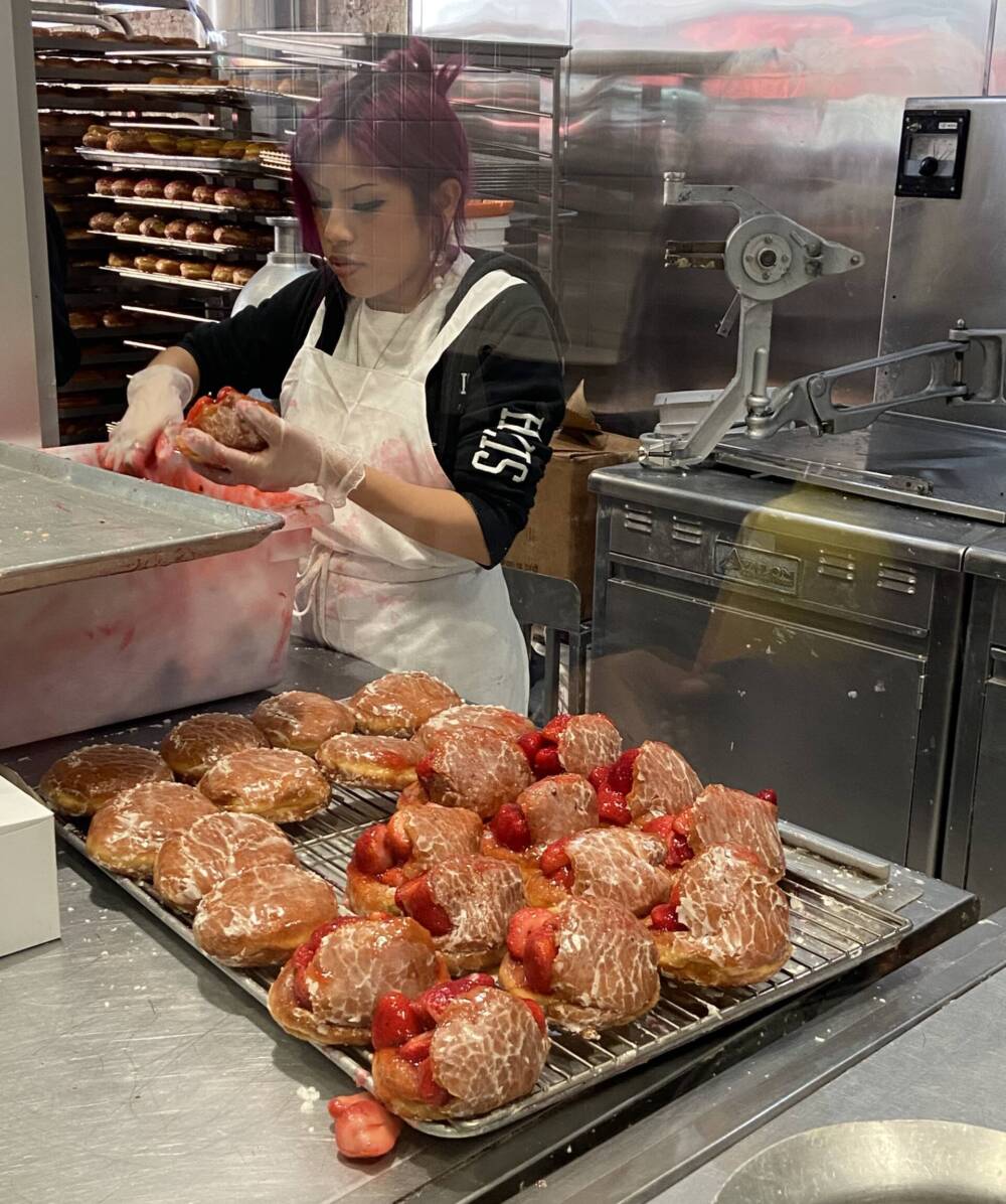 A woman stuffs donuts full of cream and strawberries at The Donut Man. (Kathy Gunst/Here & Now)