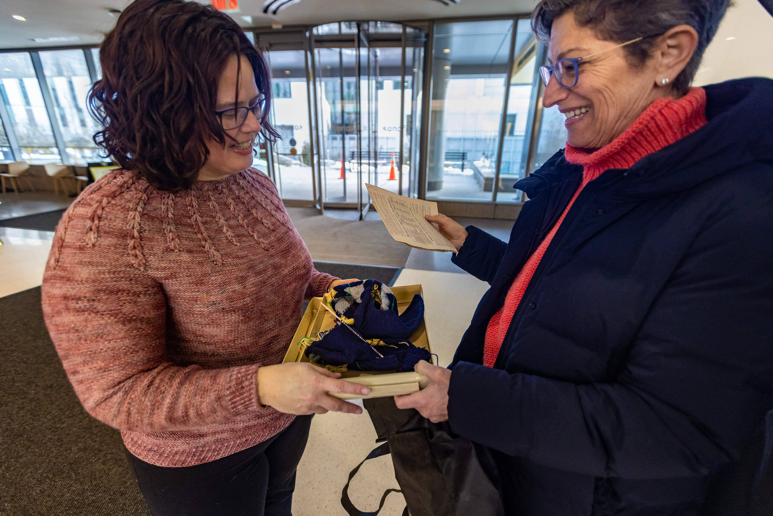 Marcia Harris gives socks her deceased mother did not finish knitting to Mariah Lopshire who will finish them. (Jesse Costa/WBUR)