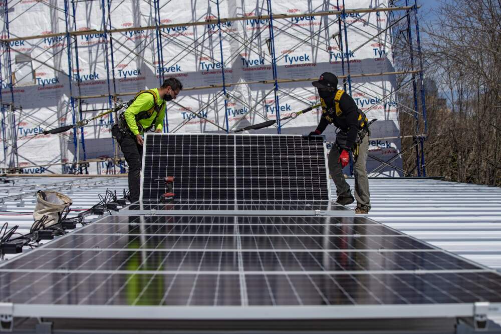 Two technicians install a solar panel on the rooftop of a Boston building. (Jesse Costa/WBUR)