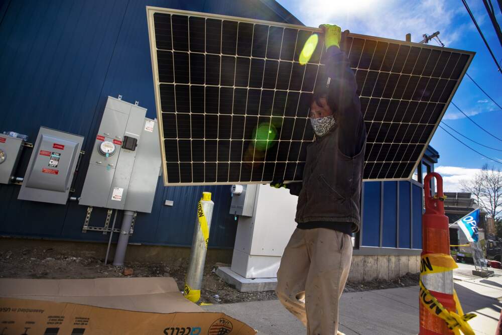 A technician walks with a solar panel during a solar panel installation on the rooftop of Boston Building Resources in Jamaica Plain. (Jesse Costa/WBUR)