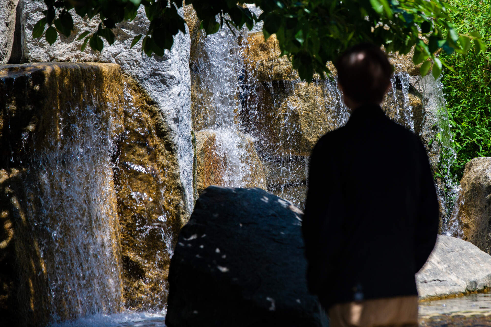 A man stands and watches the waterfall in Chinatown Park on the Rose Kennedy Greenway. (Jesse Costa/WBUR)