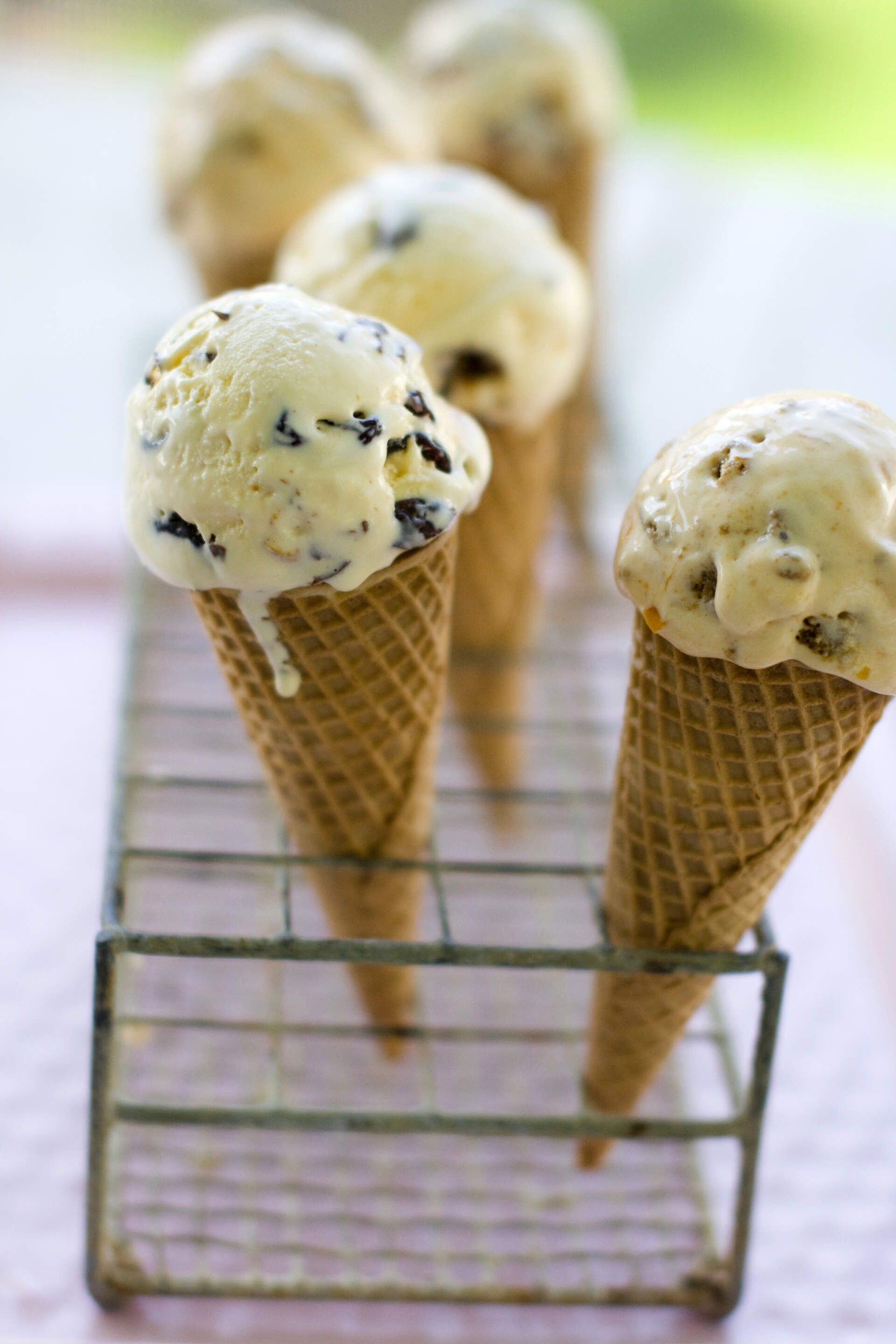 White ice cream with dark speckles melt in a waffle cone on a stand.