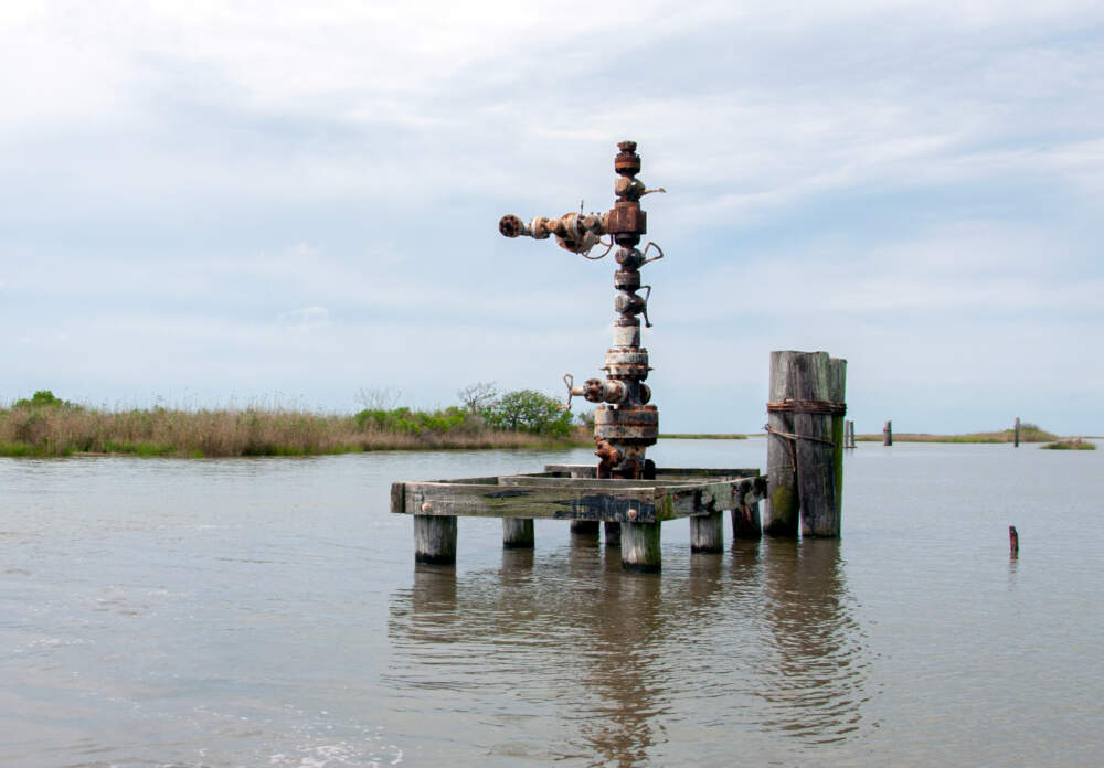 An abandoned well about a mile and a half off the coast of Buras, Louisiana, sheltered by eroding wetlands. Native American mounds are visible on the left. (Chris Bentley/Here & Now)