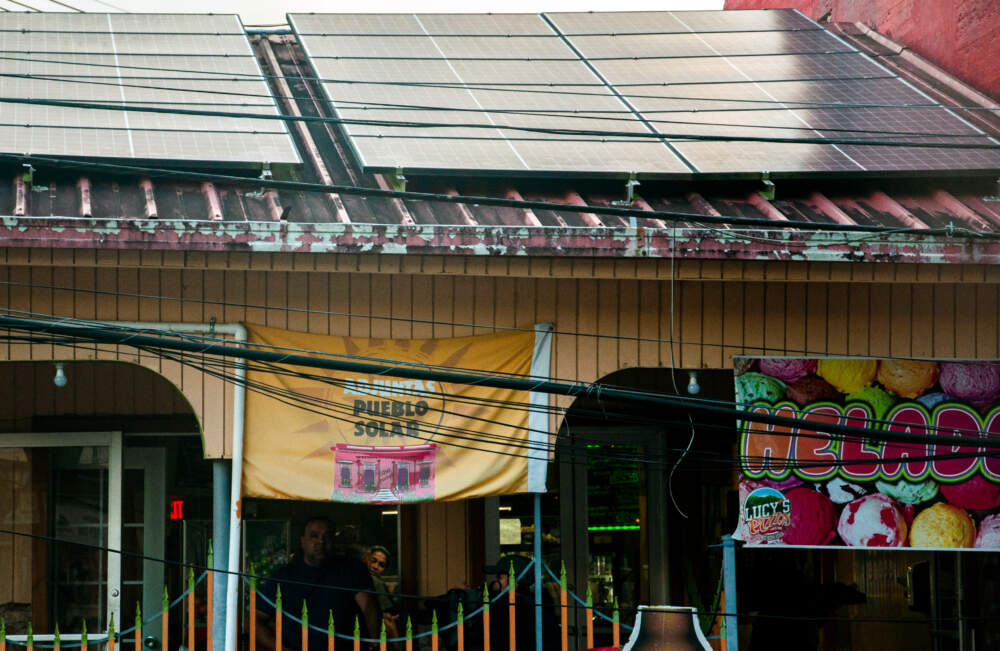 A flag reading “solar village” hangs from the patio of Lucy’s Pizza, one of the businesses in Adjuntas on the new microgrid. (Chris Bentley/Here & Now)