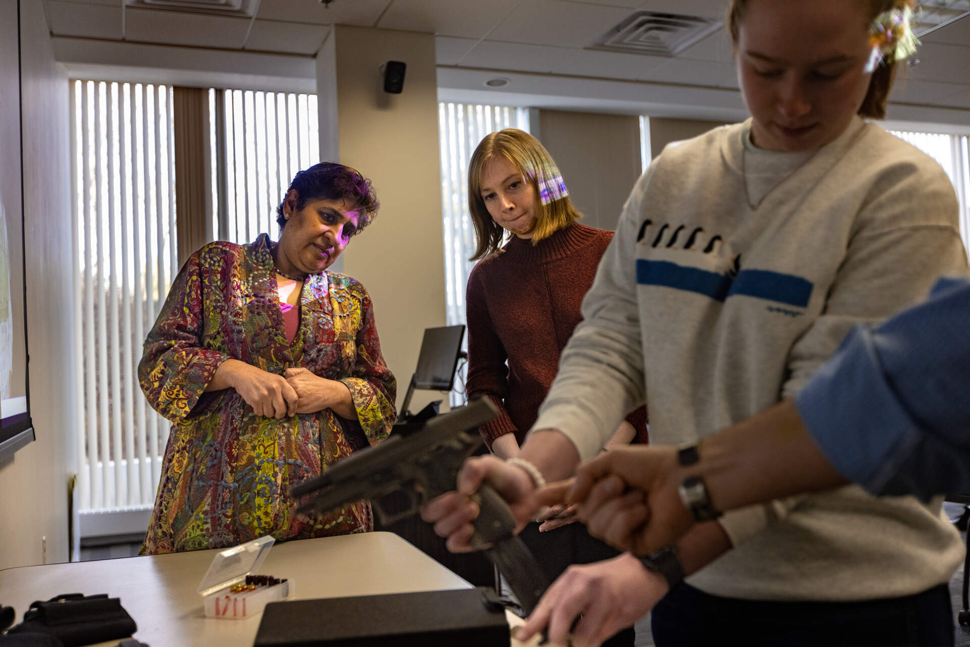 Sonia Suri and Alex Ford watch as Haley Lynch learns the mechanisms and safe handling of a gun. (Jesse Costa/WBUR)